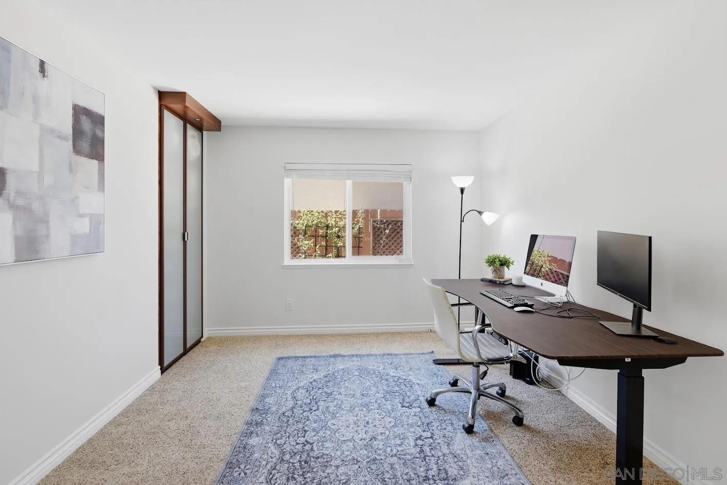 Home office with a long desk, two monitors, and a blue patterned rug.