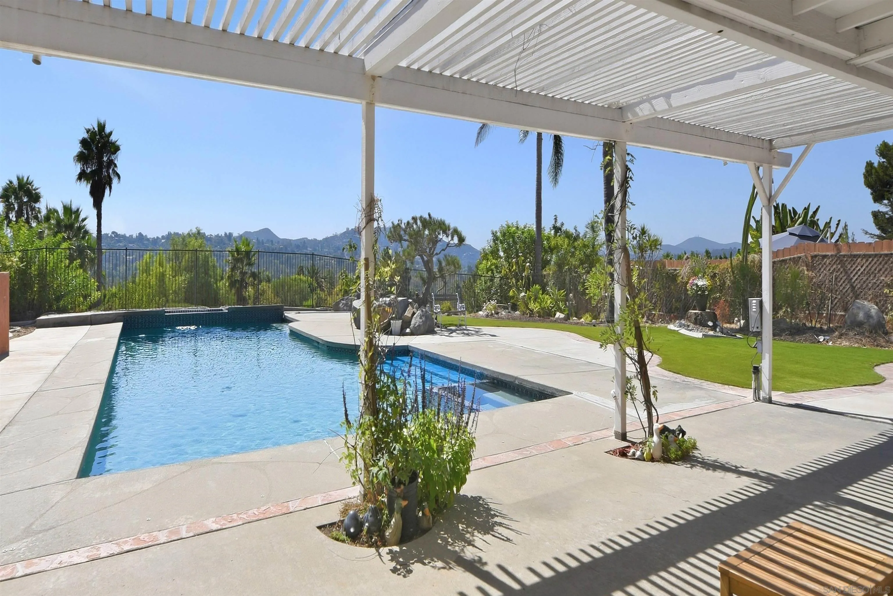 Backyard pool beneath a slatted pergola, with a landscaped lawn and distant mountain views.
