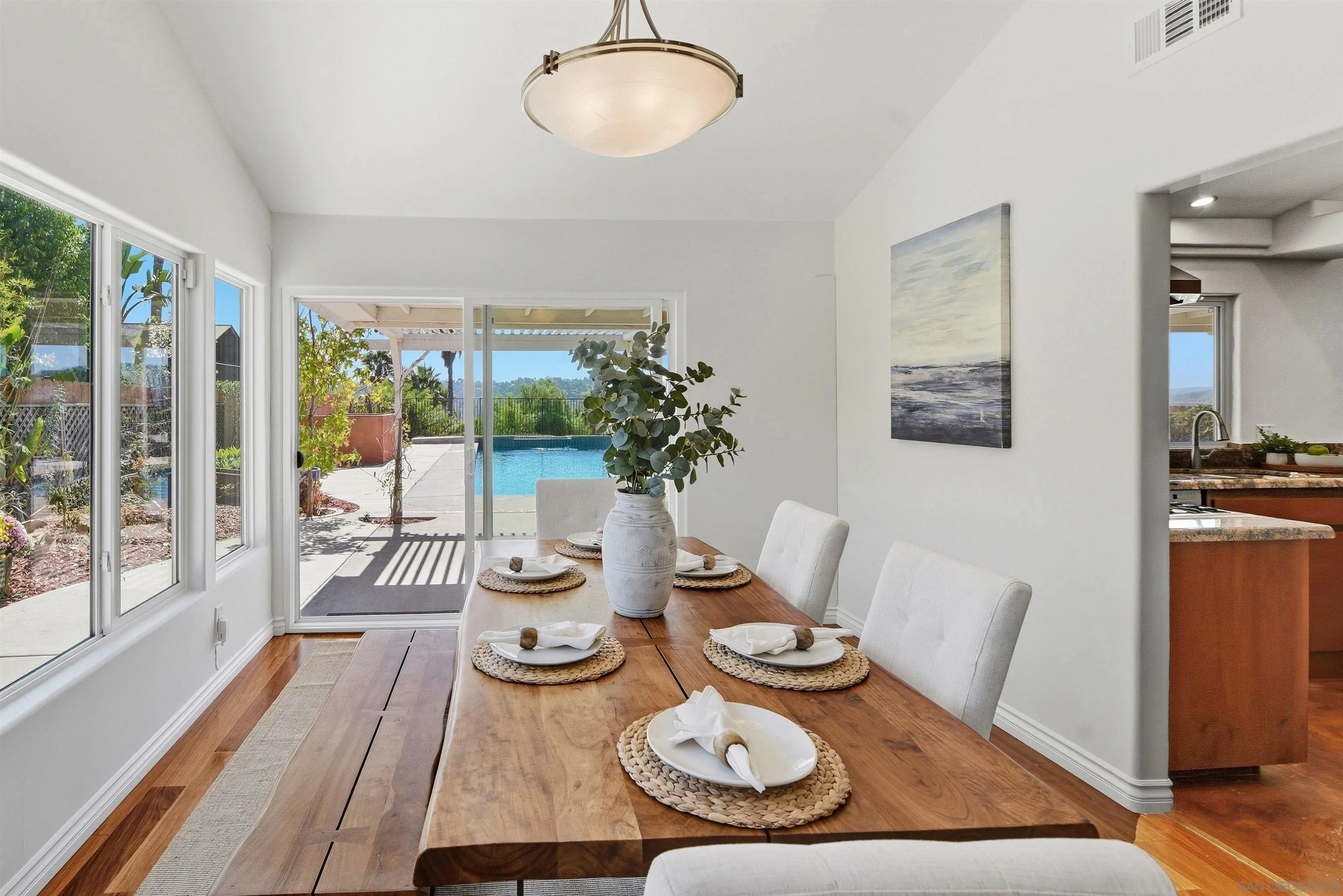 Dining room with a wooden table overlooking a patio and swimming pool.