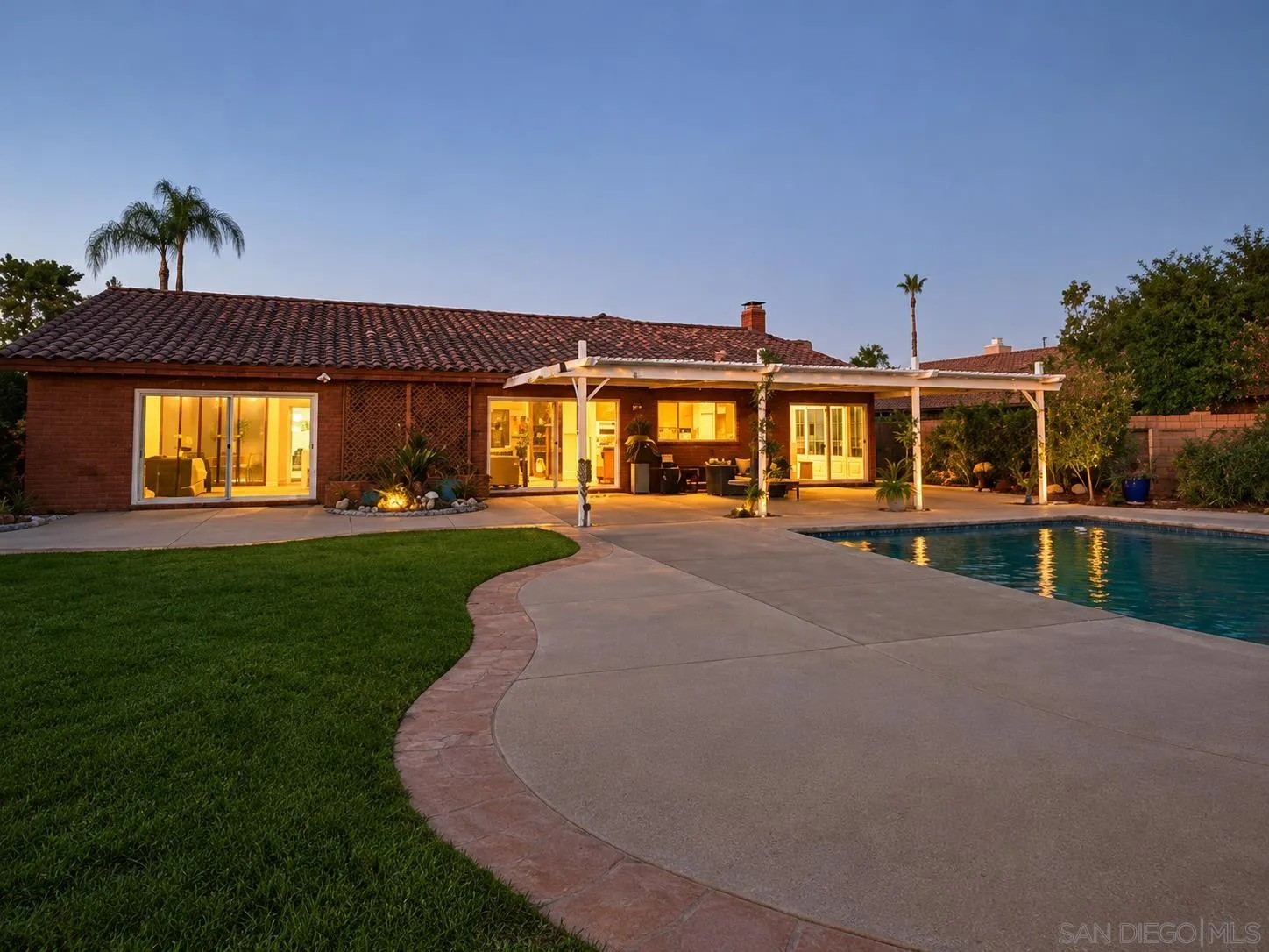 Single-story brick home at dusk with an illuminated covered patio and swimming pool.