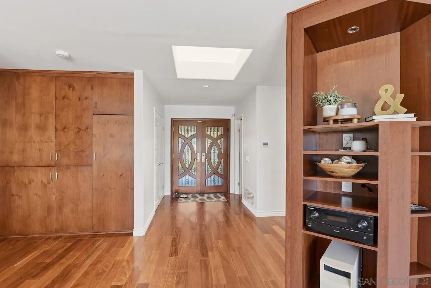 Entryway with decorative glass double doors, warm wood floors, built-in cabinetry, and a skylight.