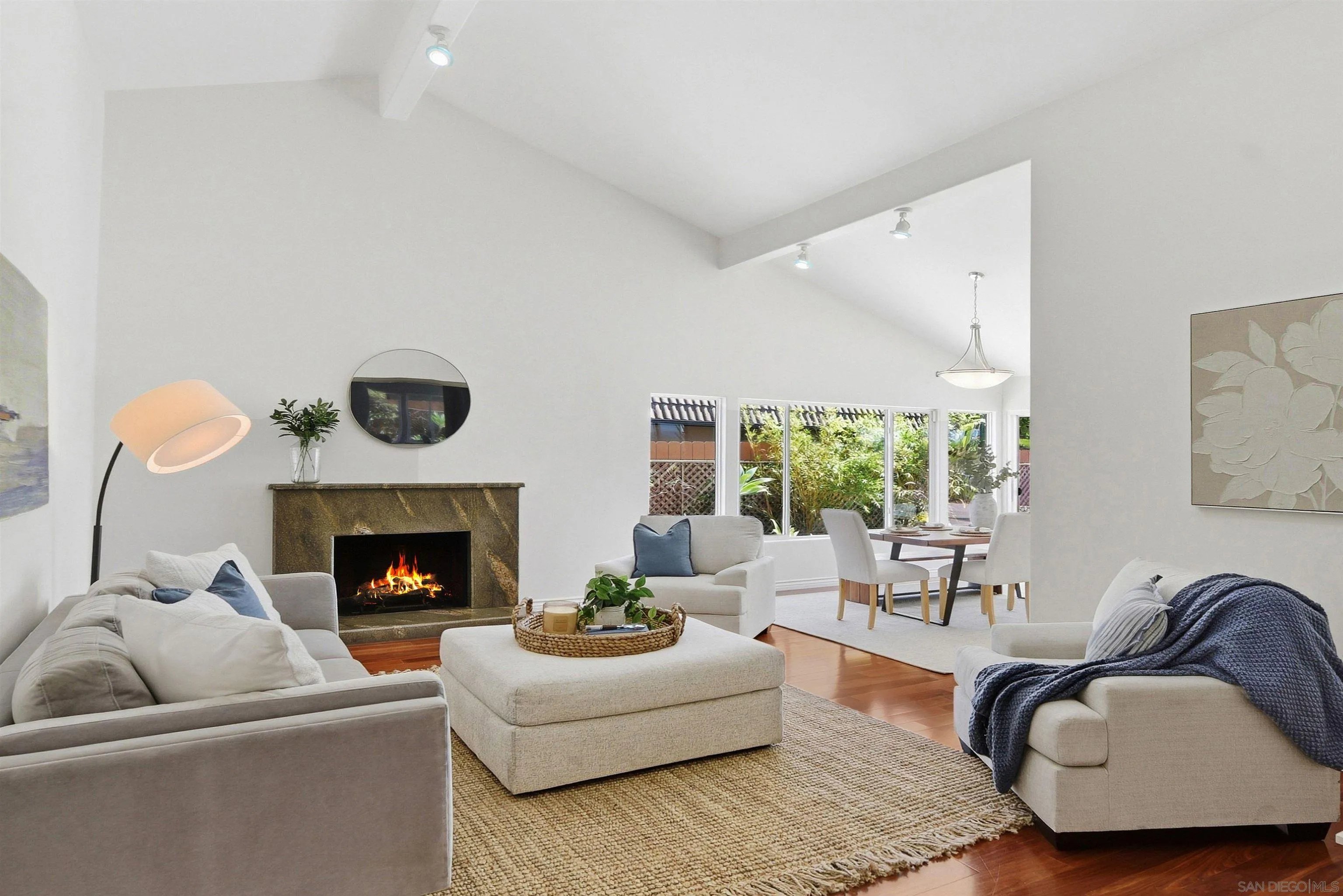 Living room with a stone fireplace, vaulted ceiling, and adjoining dining area by large windows.