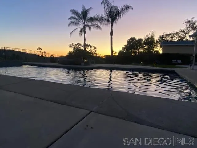 Swimming pool at dusk with rippling water and two tall palm trees.