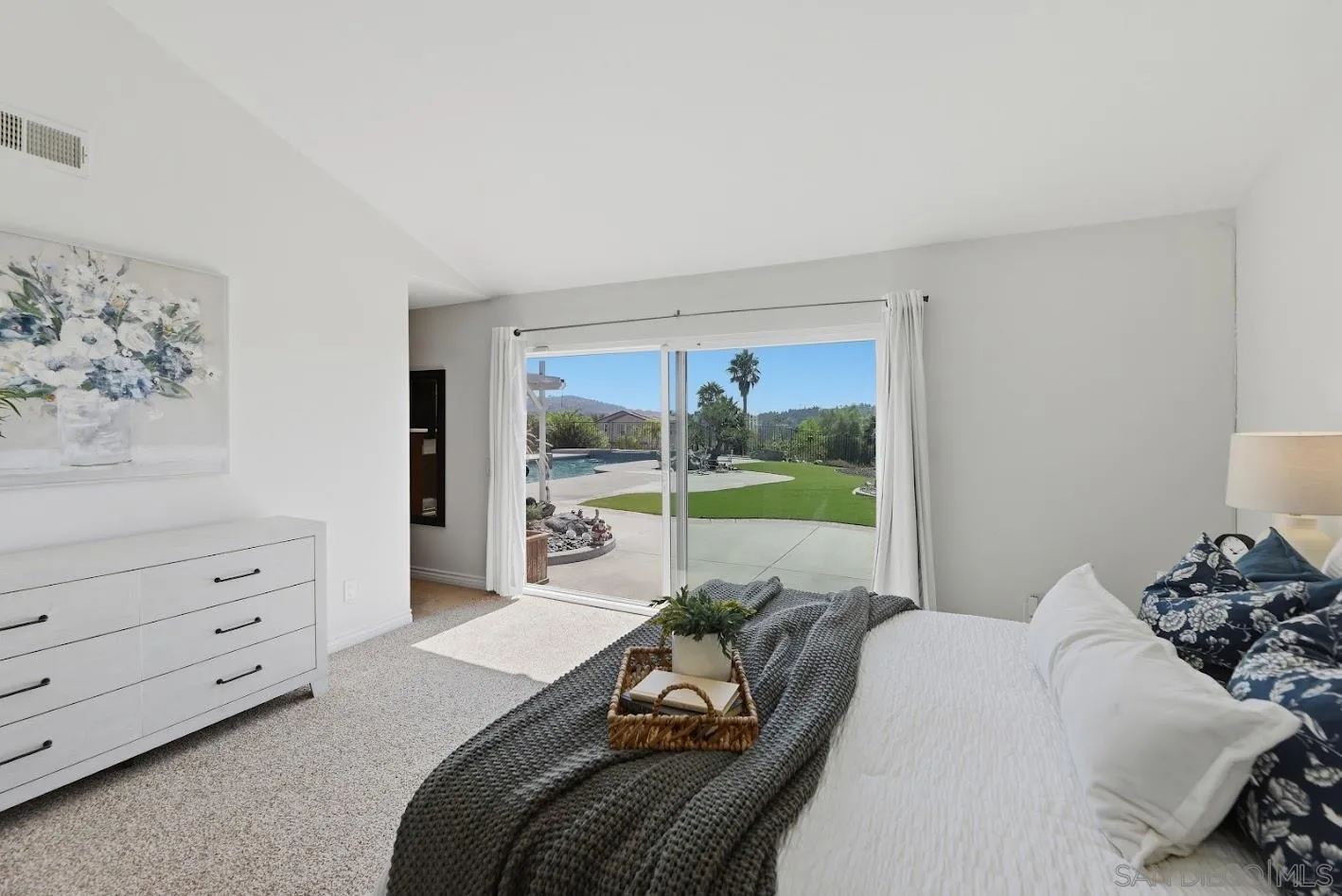 Furnished bedroom with sliding doors overlooking a backyard pool and lawn.