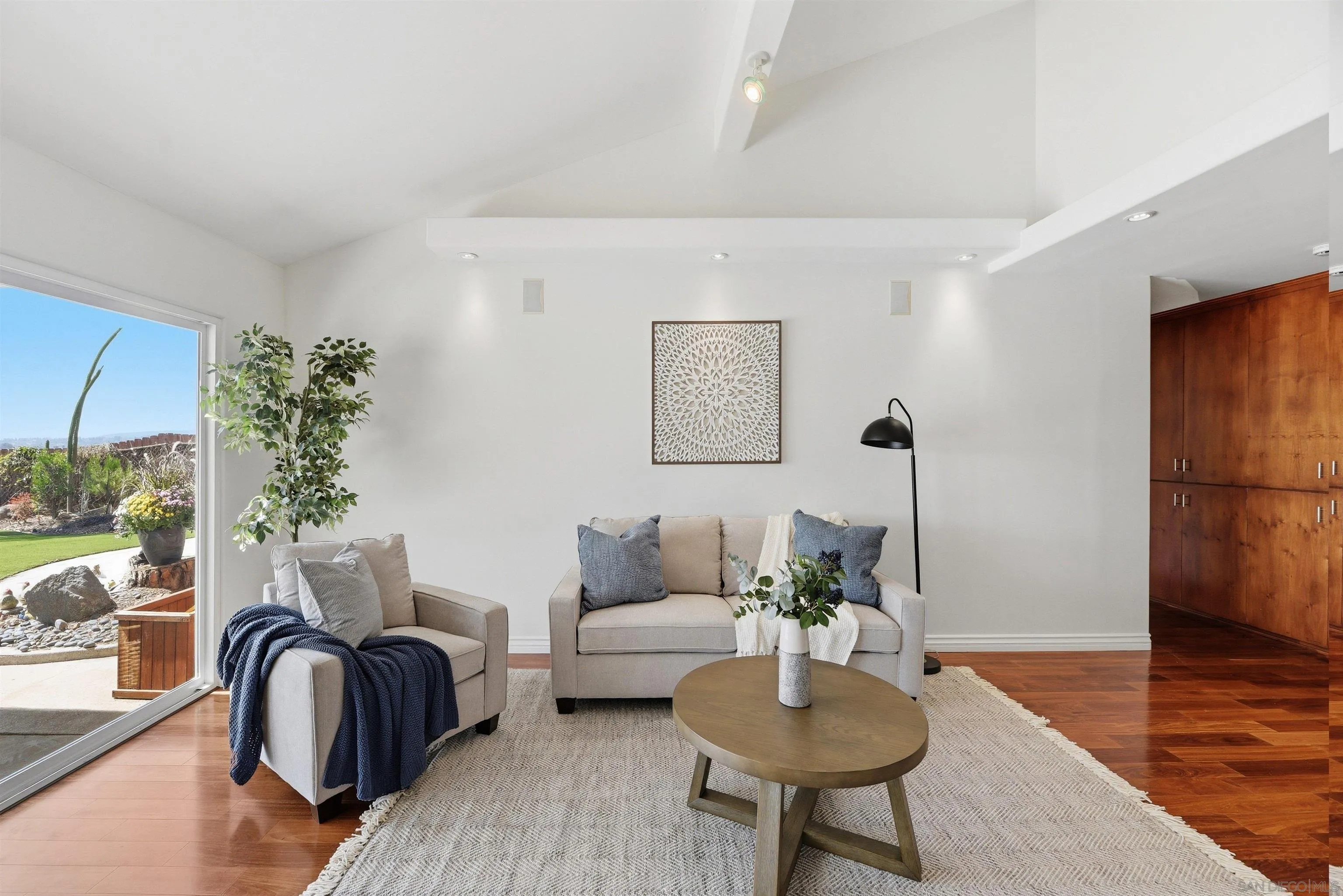 Furnished living room with gray sofas, a round coffee table, warm wood floors, and a garden view.