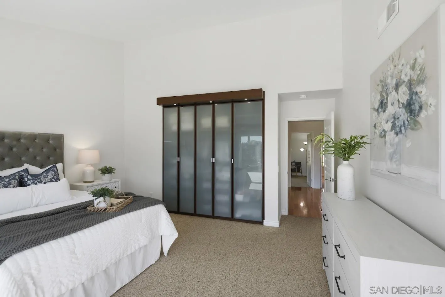 Bedroom with frosted-glass closet doors, beige carpet, and a long white dresser.