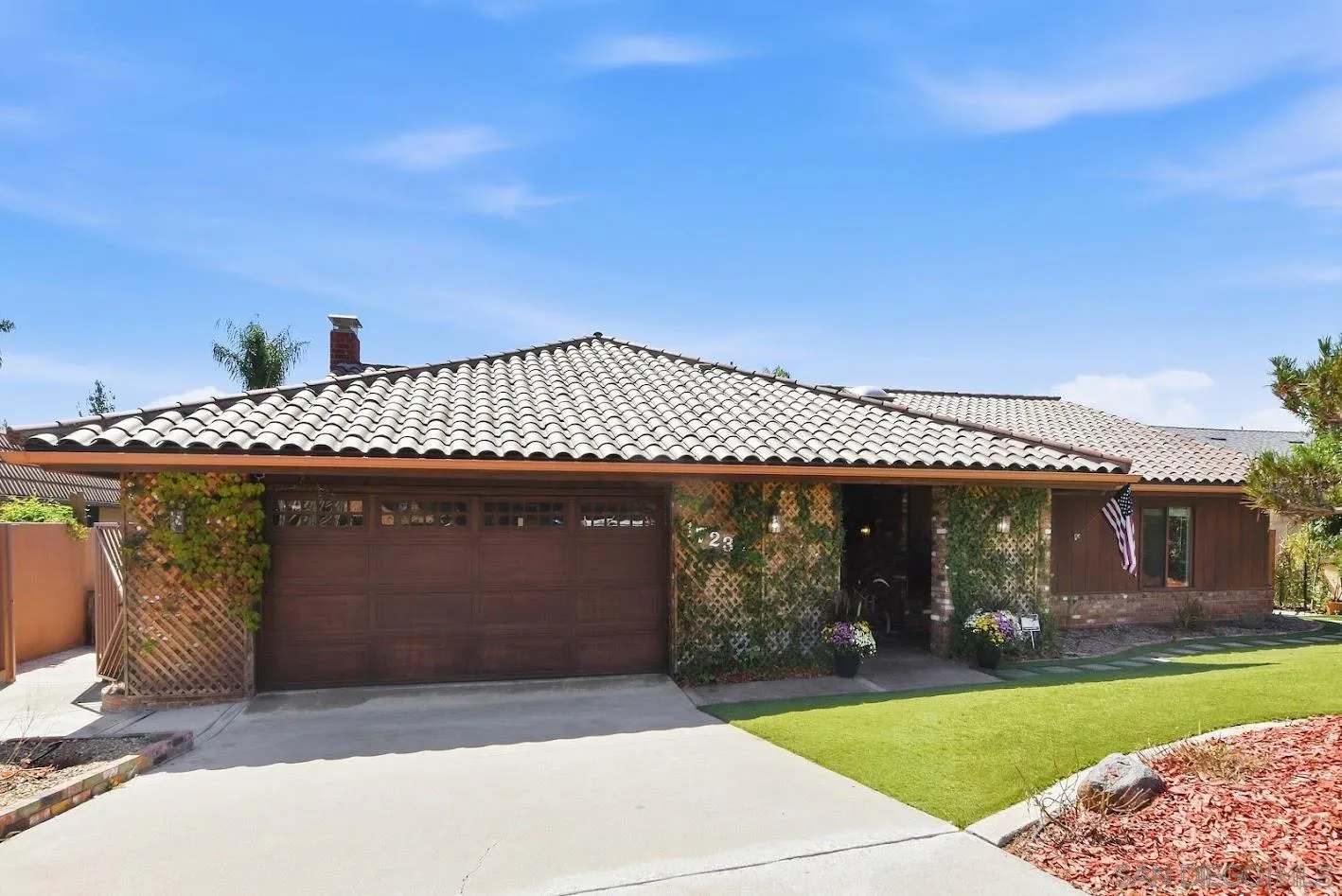 Single-story home with a tile roof, vine-covered lattice, and a broad driveway.