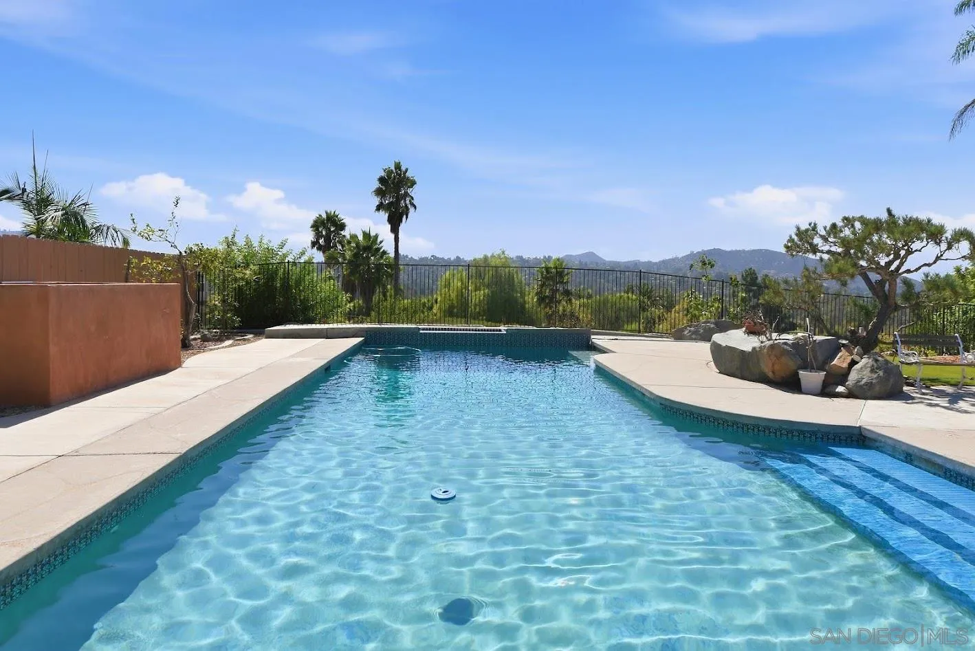 Backyard swimming pool with a concrete deck, palm trees, and distant hills.