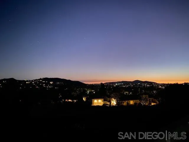 Distant city lights across rolling hills beneath a colorful dusk sky.