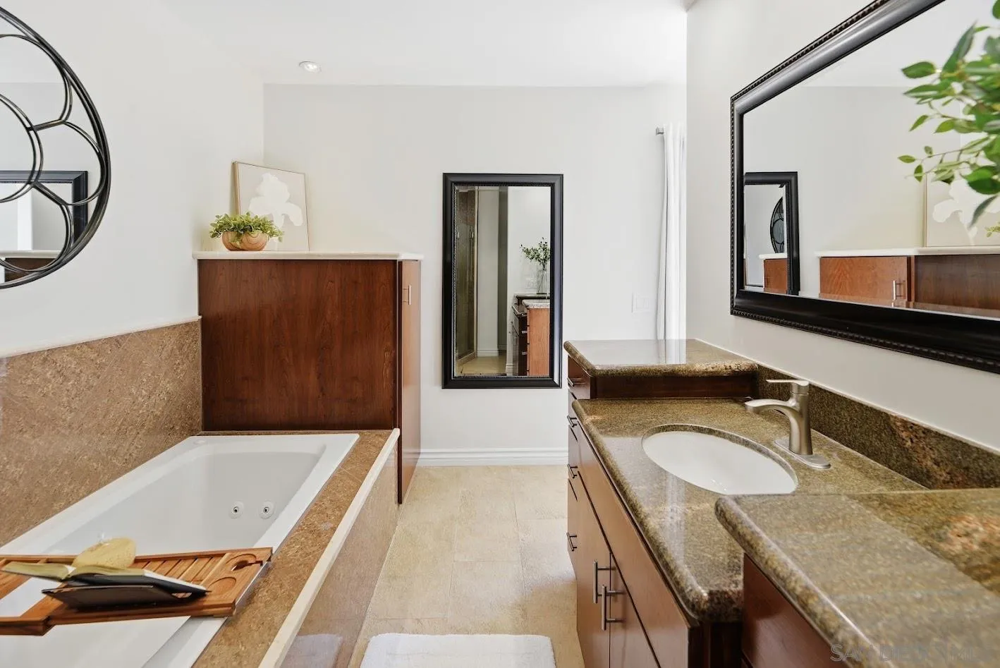 Bathroom with a soaking tub beside a wood vanity and granite countertop.