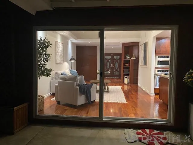 Living room with a light sofa and hardwood floors, viewed through sliding glass doors.