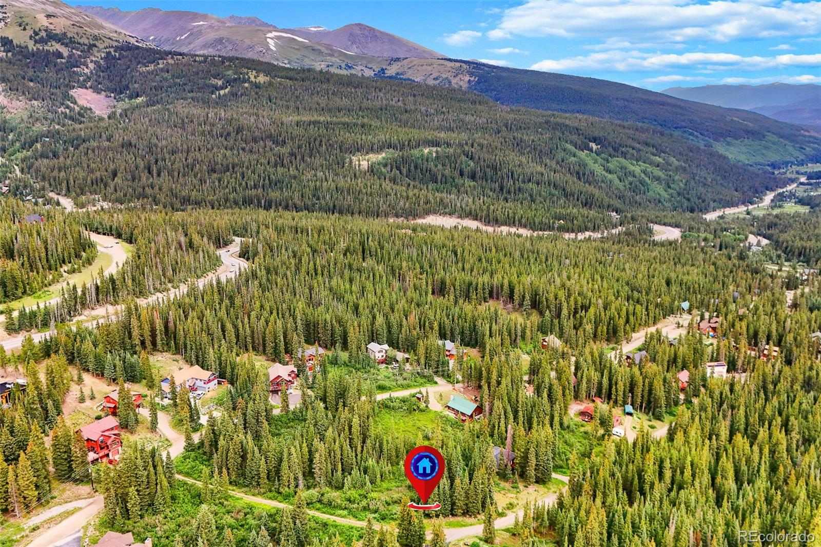 Aerial view of wooded mountain homes and winding roads, with a marker identifying the property.