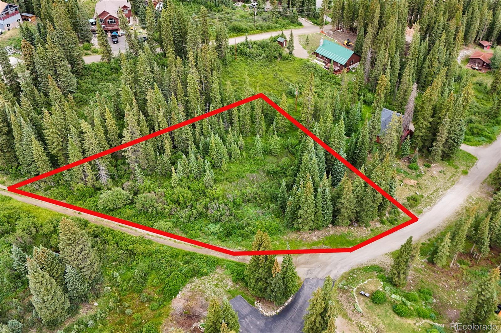 Aerial view of a wooded parcel outlined in red beside a gravel road.
