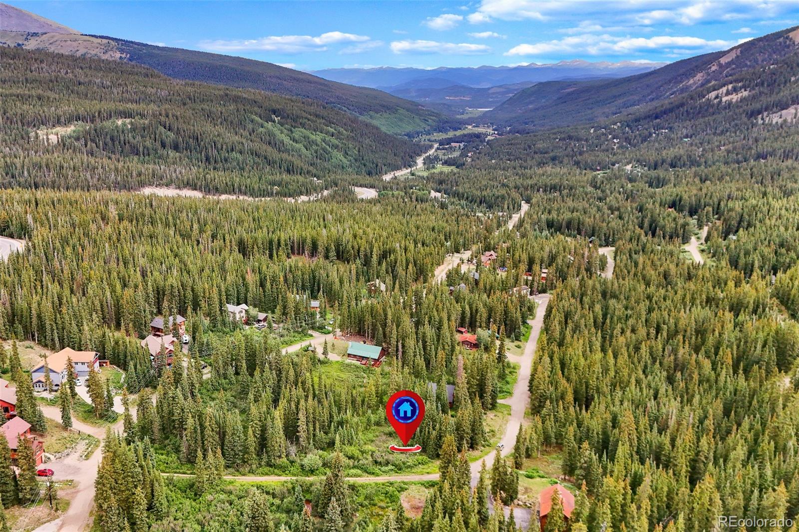 Aerial view of a forested mountain valley with scattered homes, winding roads, and distant peaks.