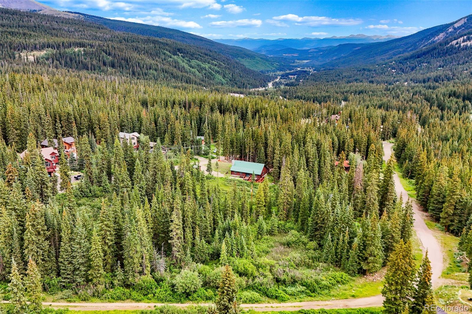 Aerial view of homes among dense evergreen forest, with a mountain valley stretching into the distance.