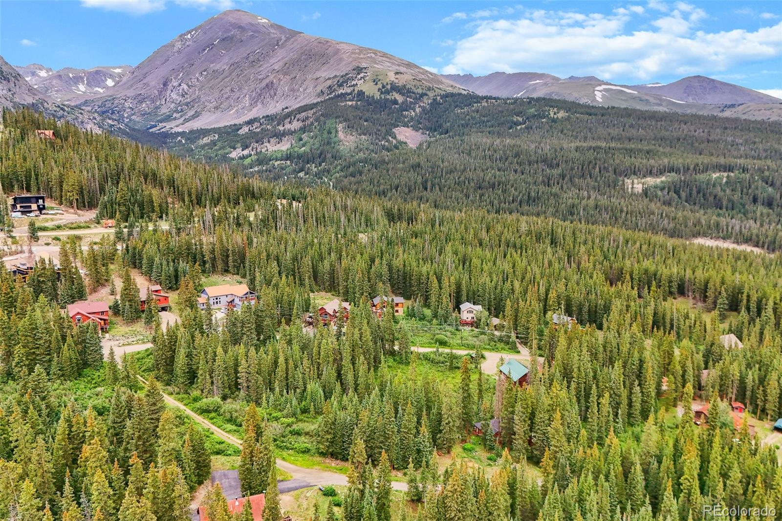 Mountain community among dense evergreen forest, with scattered homes and rugged peaks in the distance.