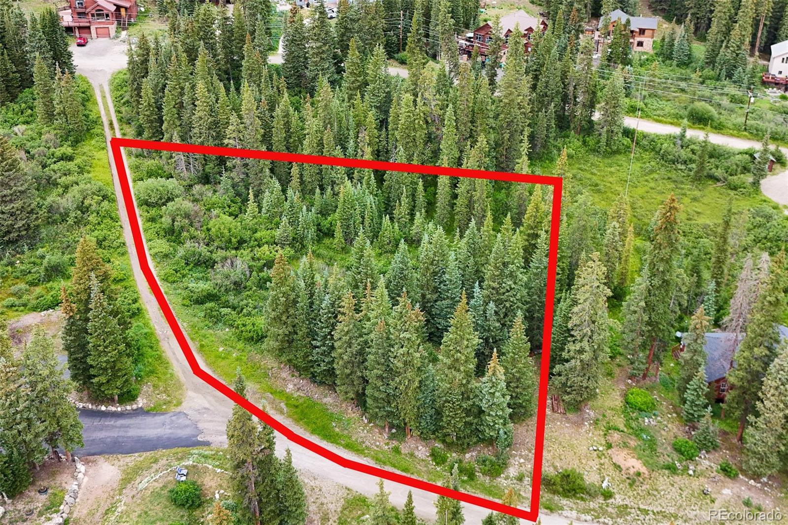 Aerial view of a wooded vacant lot outlined in red beside a dirt road.