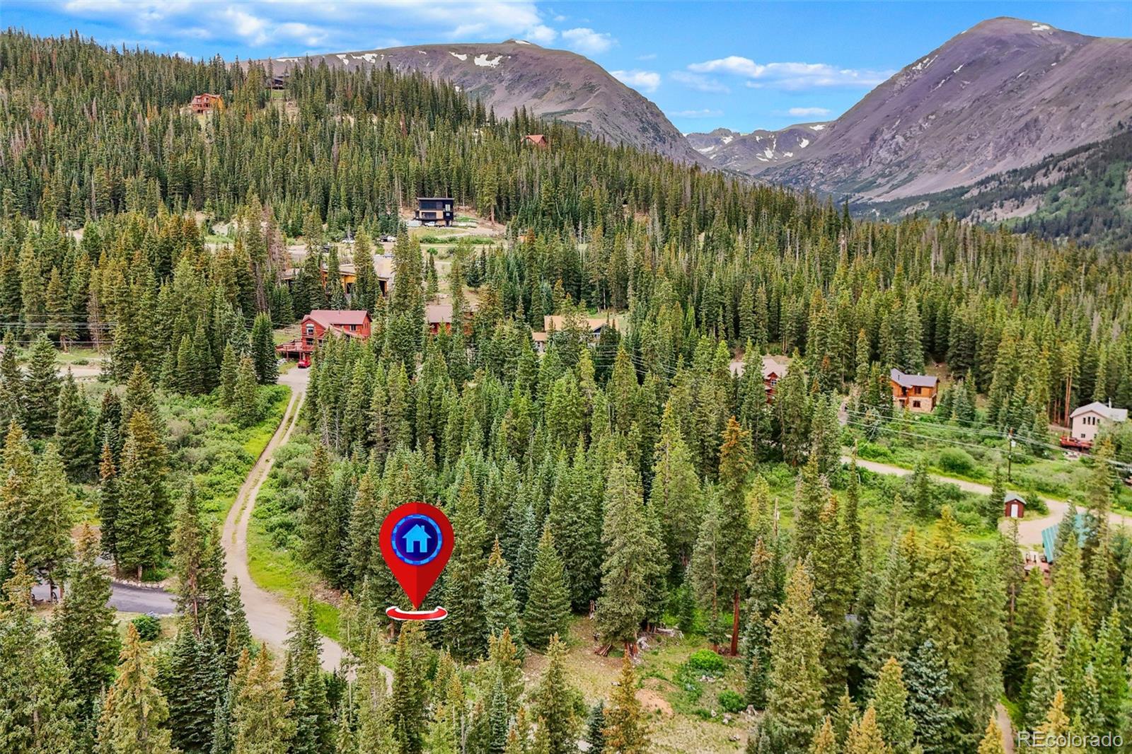 Aerial view of a mountain property among evergreen forest, with nearby cabins and rugged peaks.