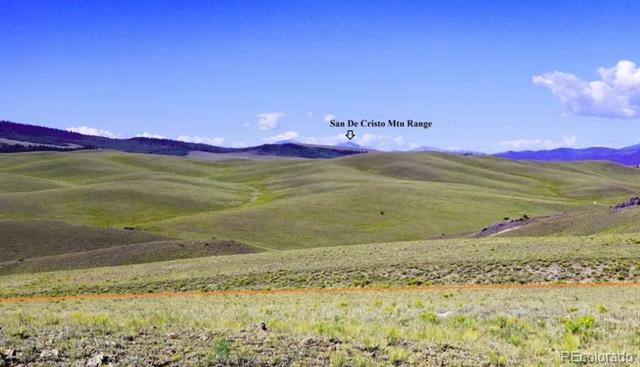 Open rolling grassland with the distant San De Cristo mountain range beneath a blue sky.