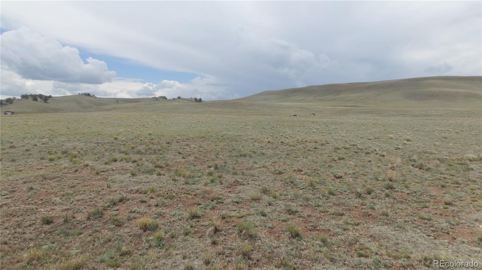Open, sparsely grassed land with rolling hills and a small outbuilding beneath a cloudy sky.