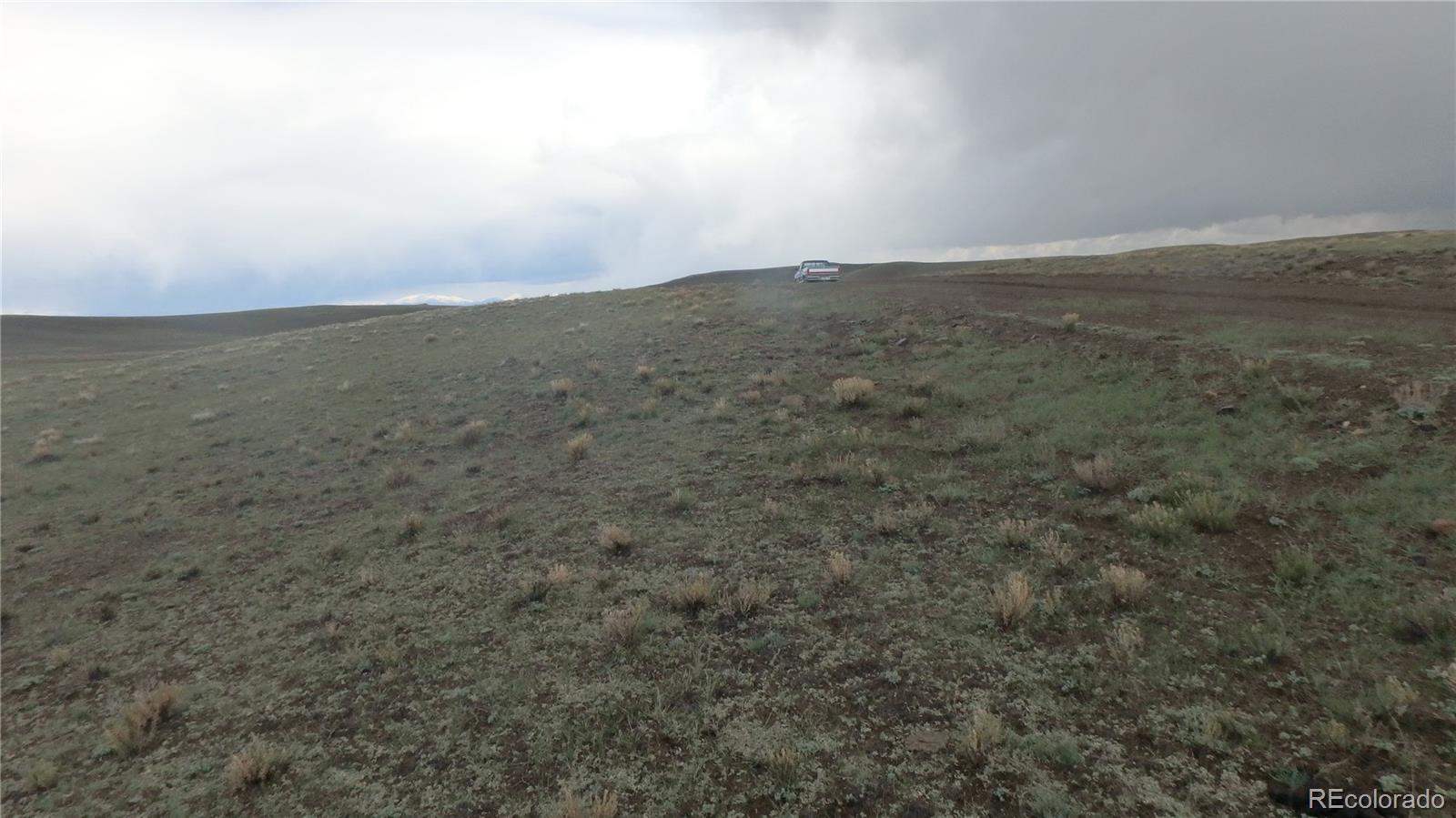 Undeveloped grassy hillside with sparse shrubs and a vehicle near the ridge.