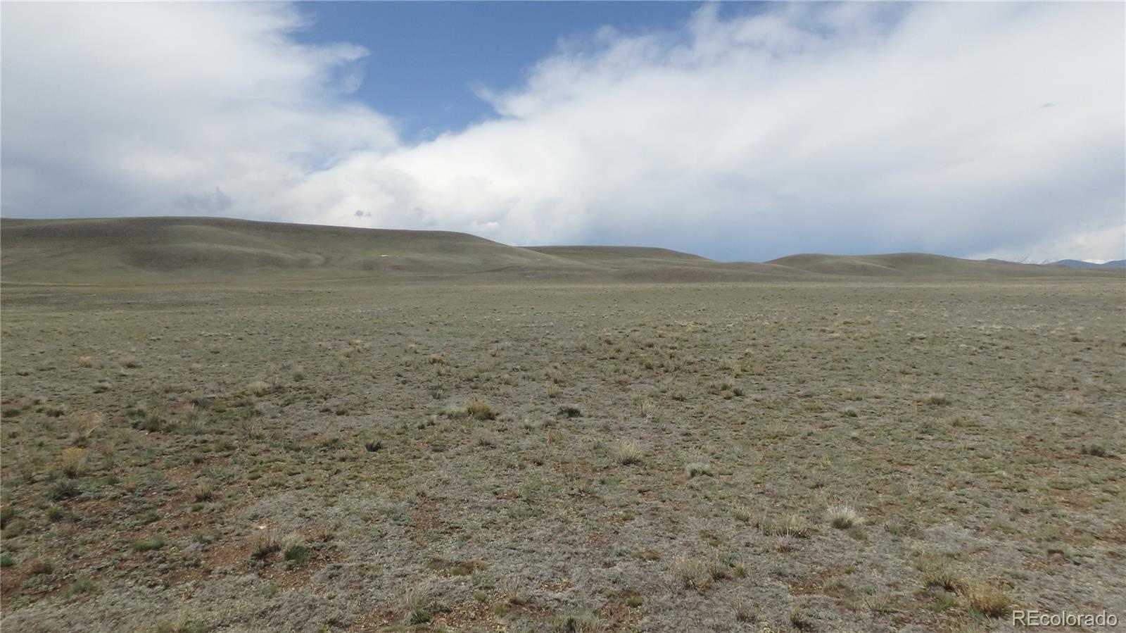 Open, sparsely vegetated land stretches toward rolling hills beneath a cloudy sky.