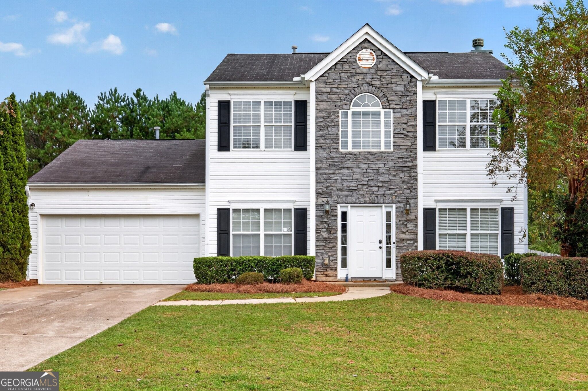 Two-story white house with a stone entry facade, black shutters, and an attached two-car garage.