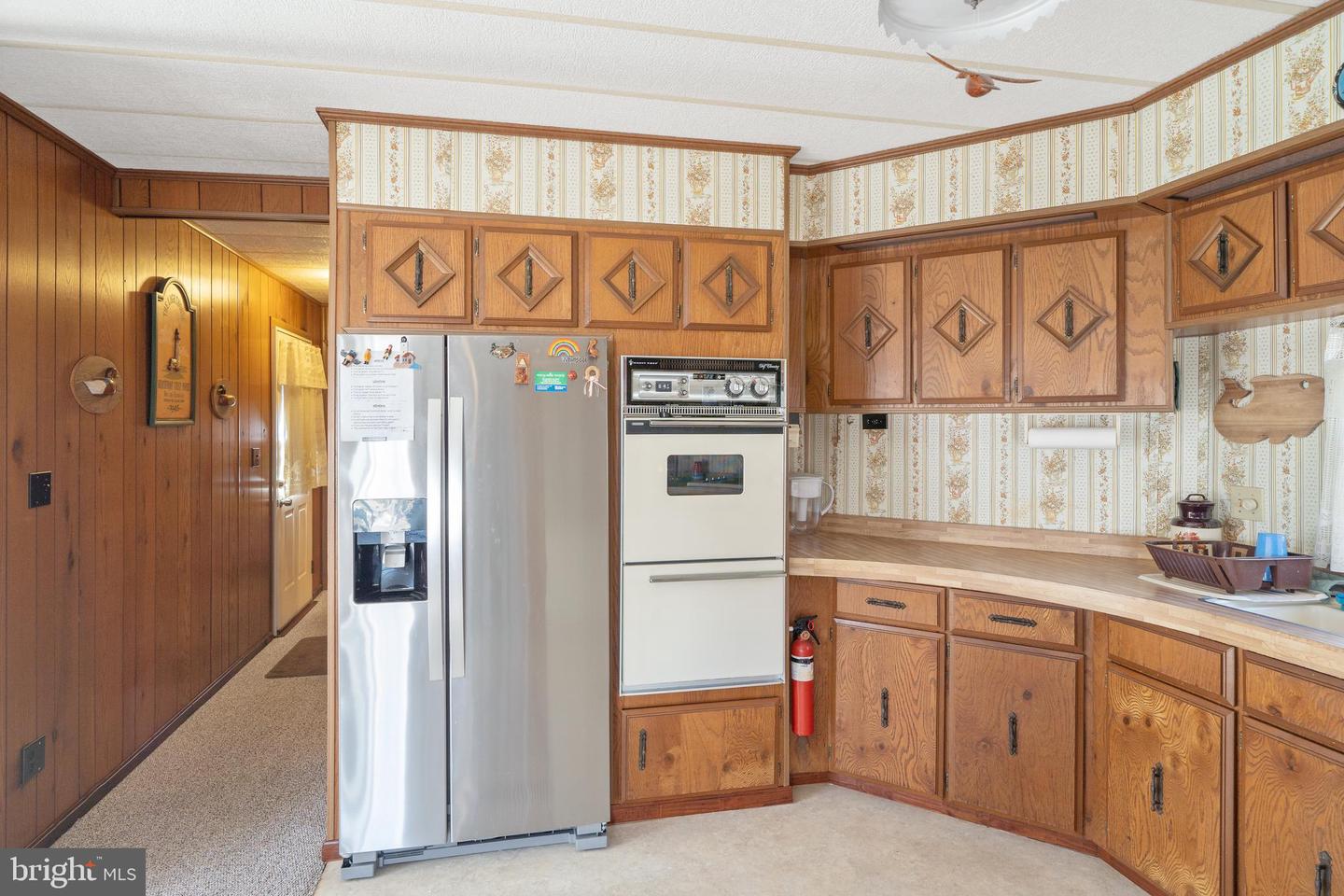 Kitchen with honey-colored wood cabinetry, patterned wallpaper, and a stainless steel refrigerator.