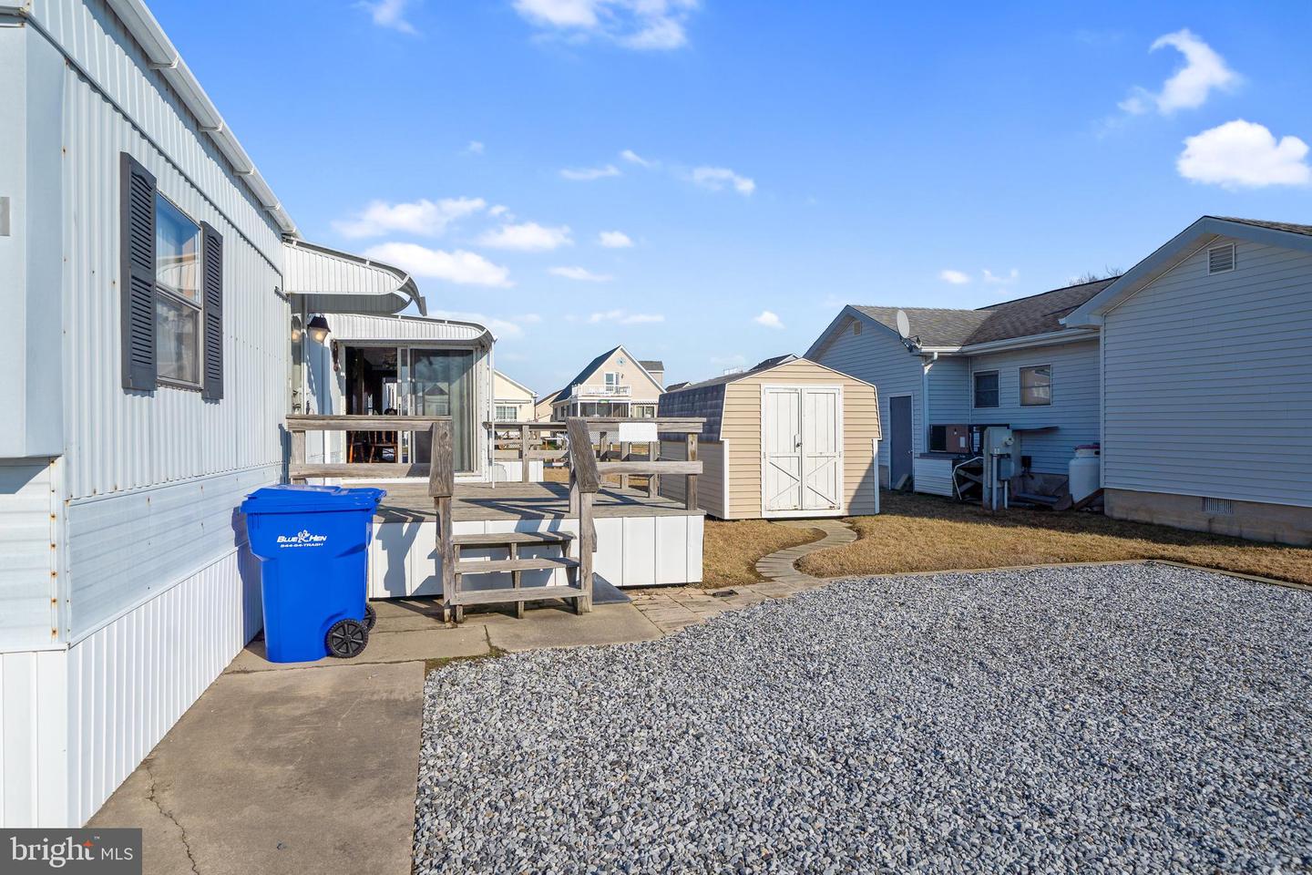 Home exterior with a raised deck, gravel yard, and small storage shed.