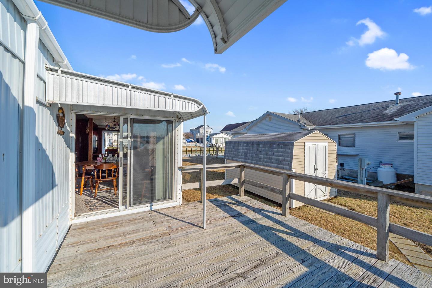 Wooden deck with a metal awning, sliding glass door, railing, and small shed.