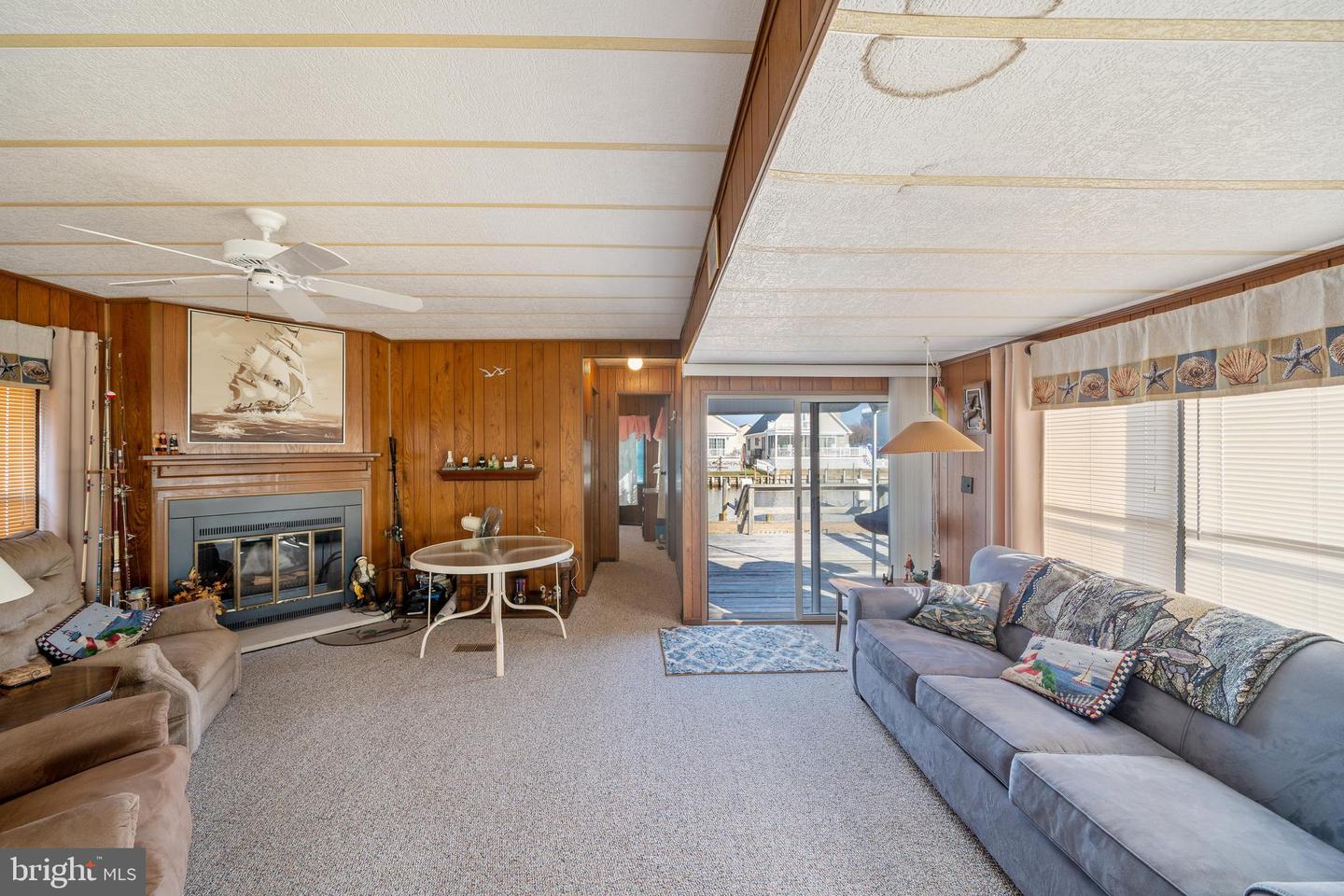 Living room with a fireplace and wood-paneled walls, opening onto a canal-side deck.