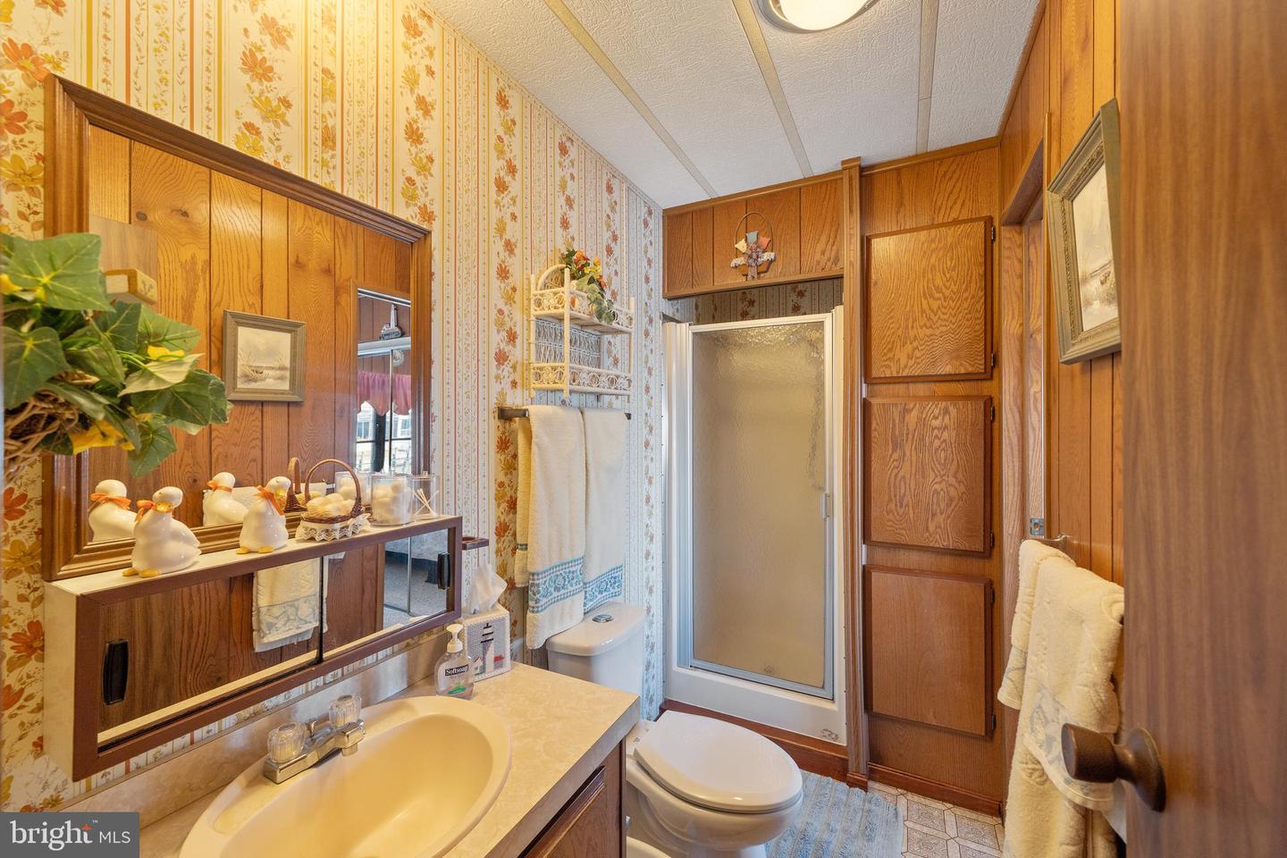Bathroom with floral wallpaper, wood cabinetry, a vanity, and a frosted-glass shower.