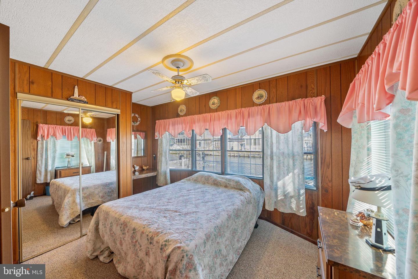 Bedroom with mirrored closet doors, wood-paneled walls, and a floral bedspread.