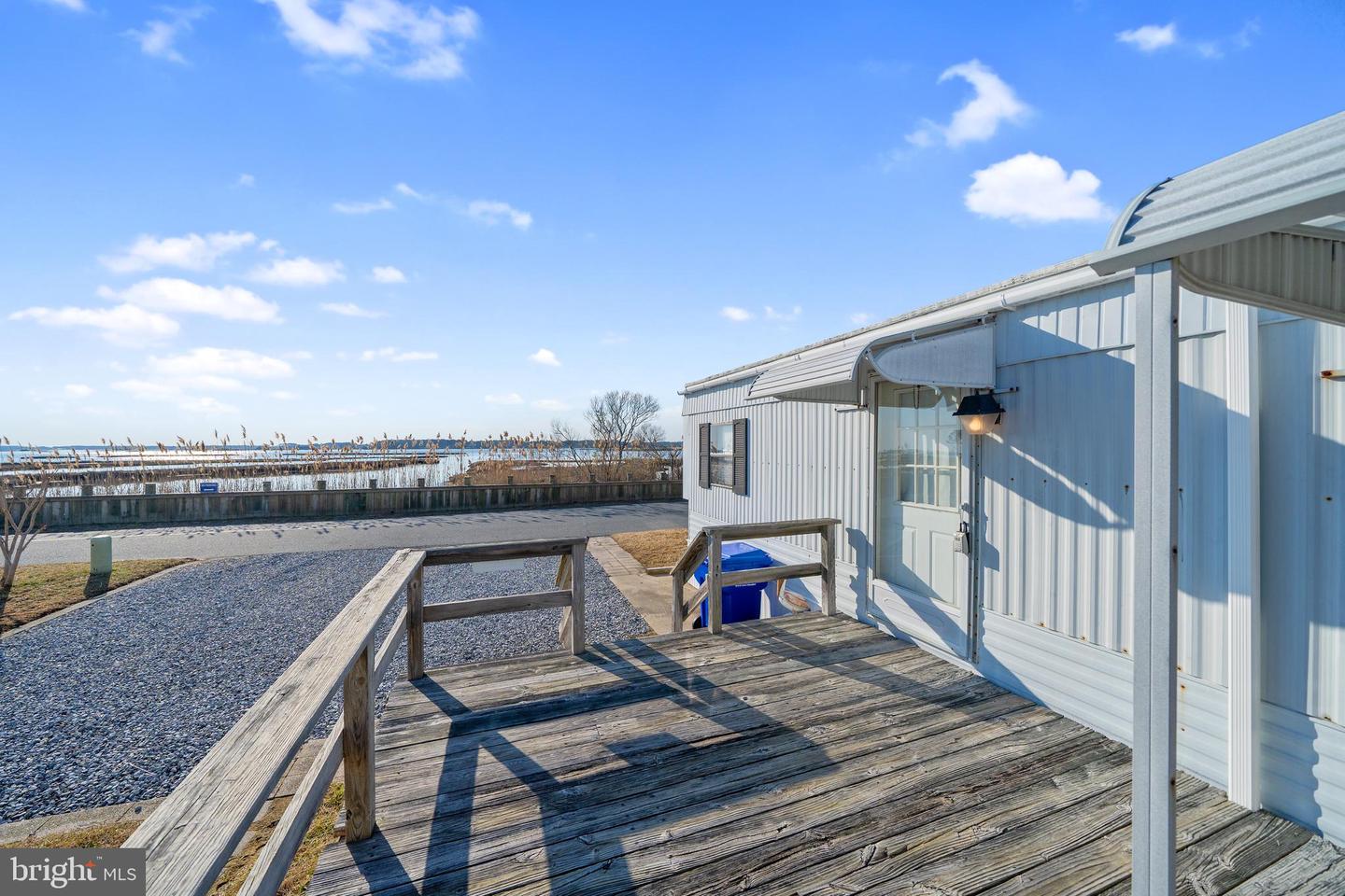 Light-colored metal-sided property with a wooden deck overlooking water.