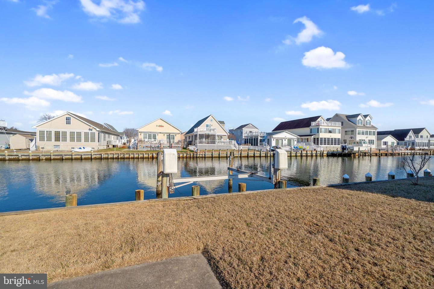 Waterfront canal view toward neighboring homes, with a boat lift and grassy bank in the foreground.