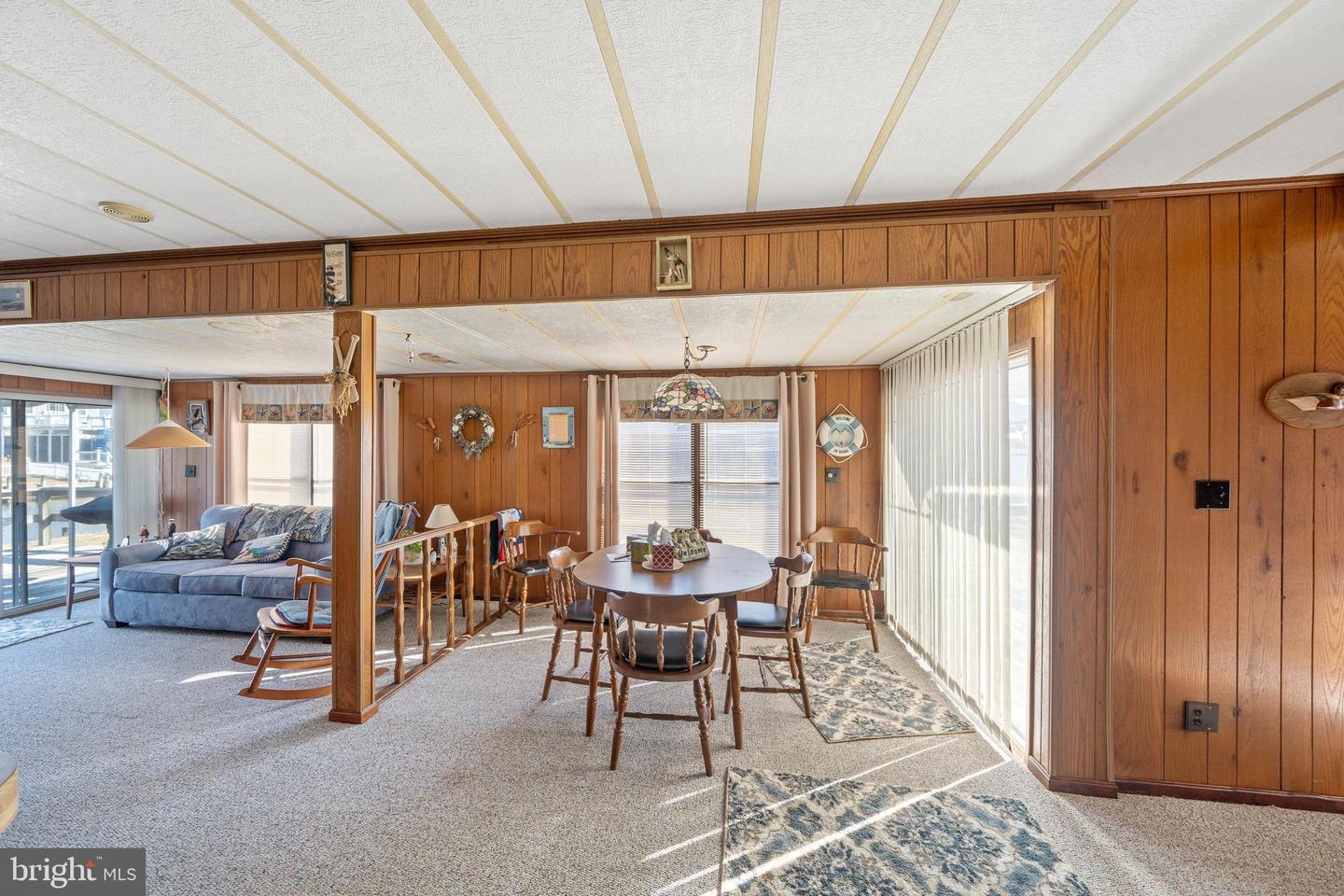 Dining and living area with wood-paneled walls, round table, patterned rugs, and blue sofa.