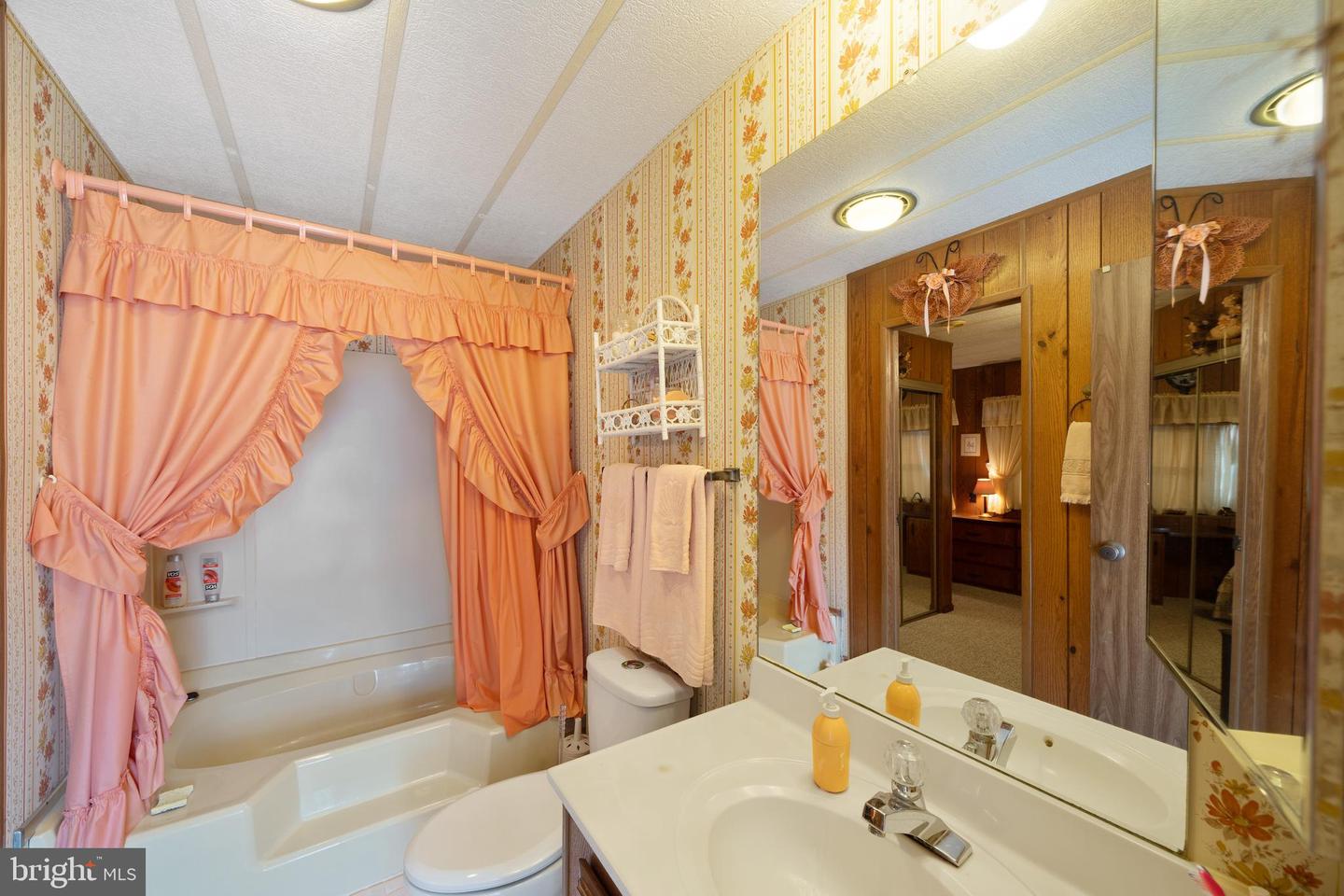 Bathroom with a bathtub, peach ruffled curtains, floral wallpaper, and a large mirrored vanity.