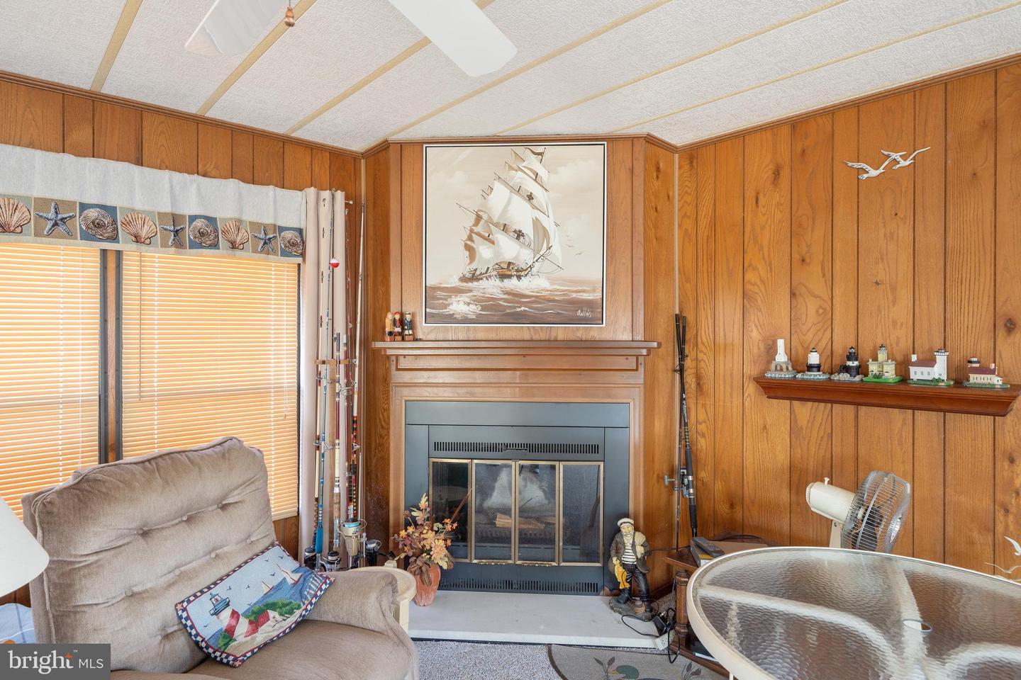 Living room with a wood-paneled fireplace, sailing ship painting, and glass-top table.