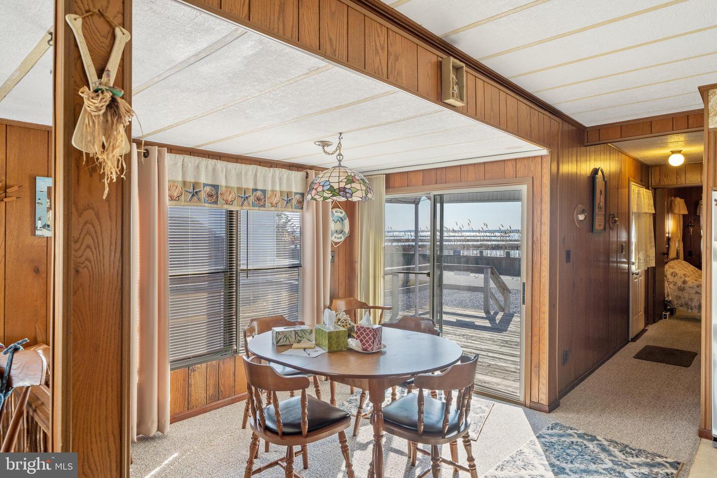 Dining area with wood-paneled walls, a round table, and sliding doors overlooking marshland and water.