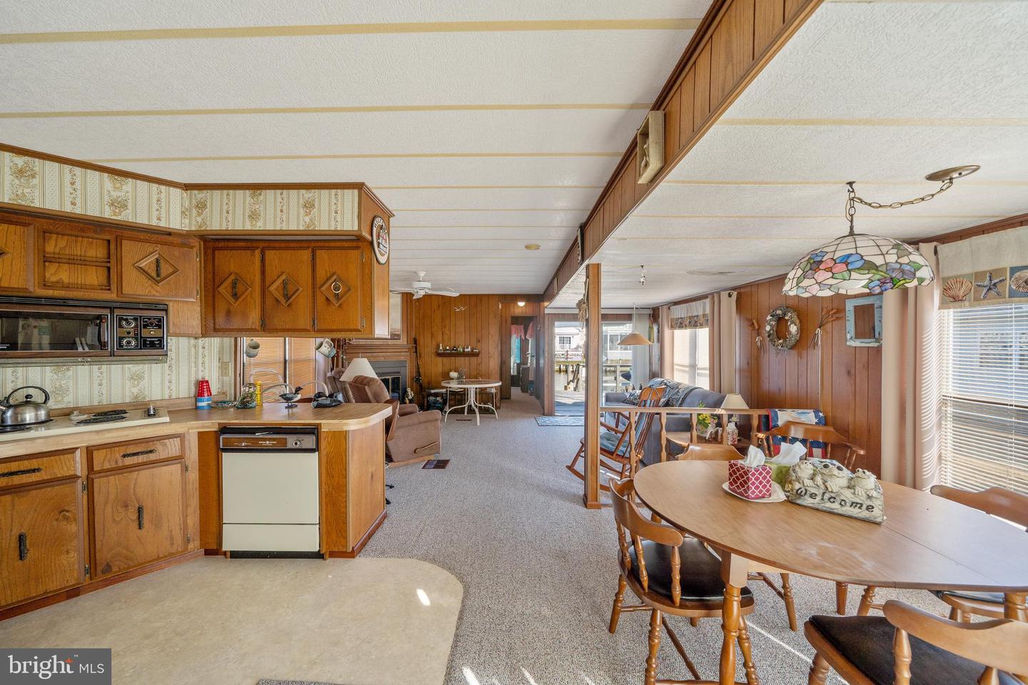 Open-plan kitchen and dining area with wood cabinetry, carpet, and a stained-glass pendant light.