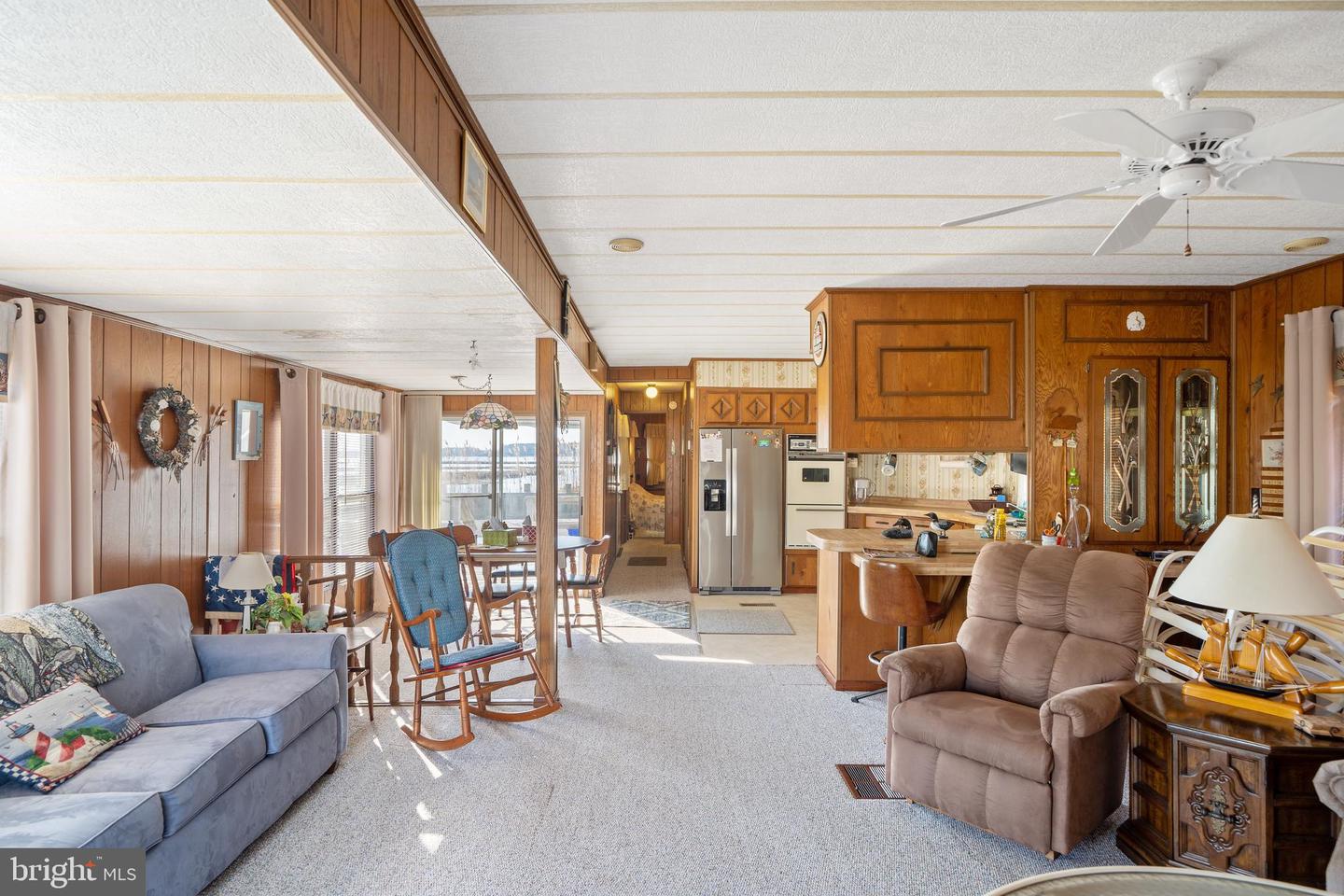 Living room opening to a dining area and kitchen, with wood-paneled walls and cabinetry.