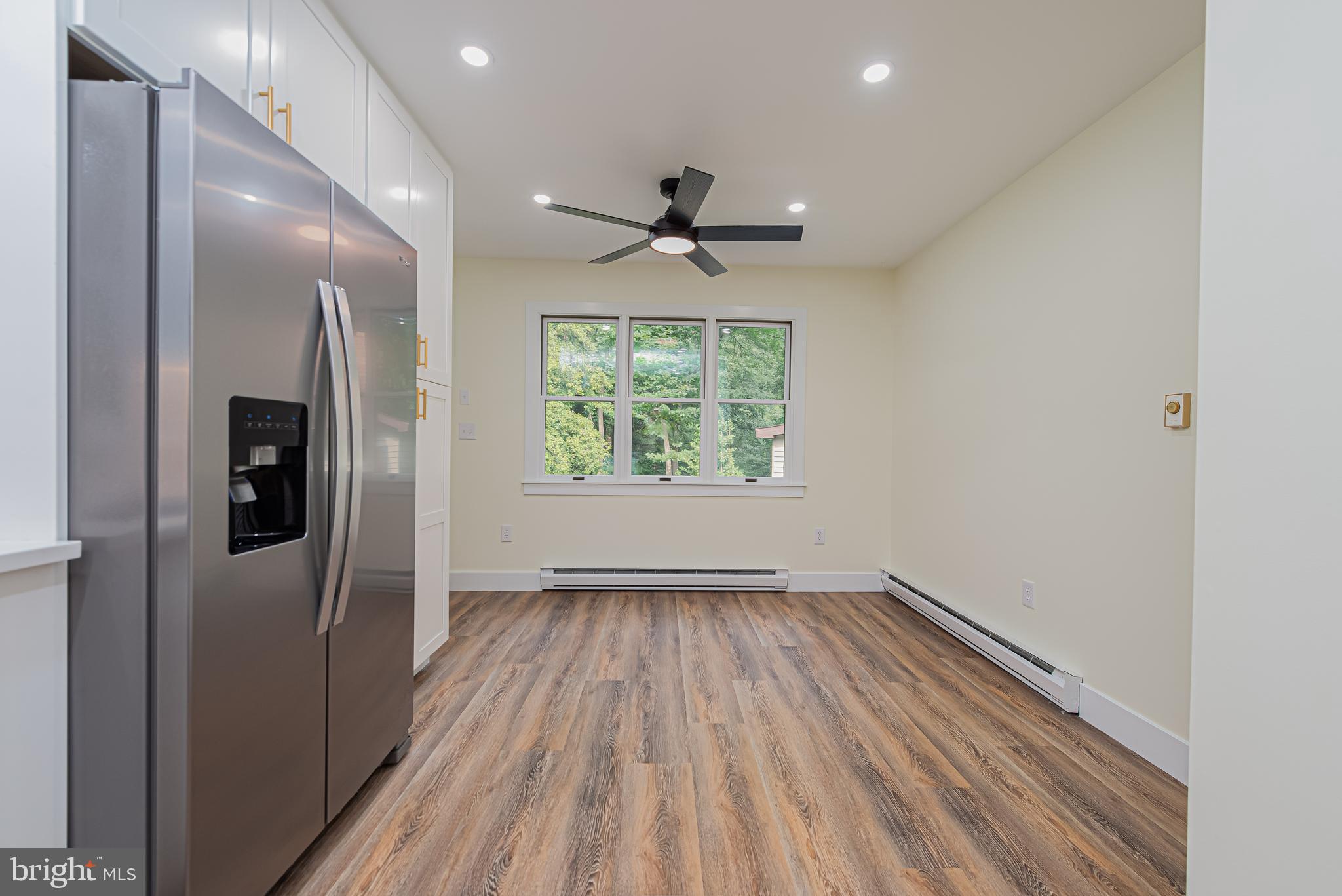 Unfurnished kitchen with a stainless steel refrigerator, wood-look flooring, and a window overlooking trees.