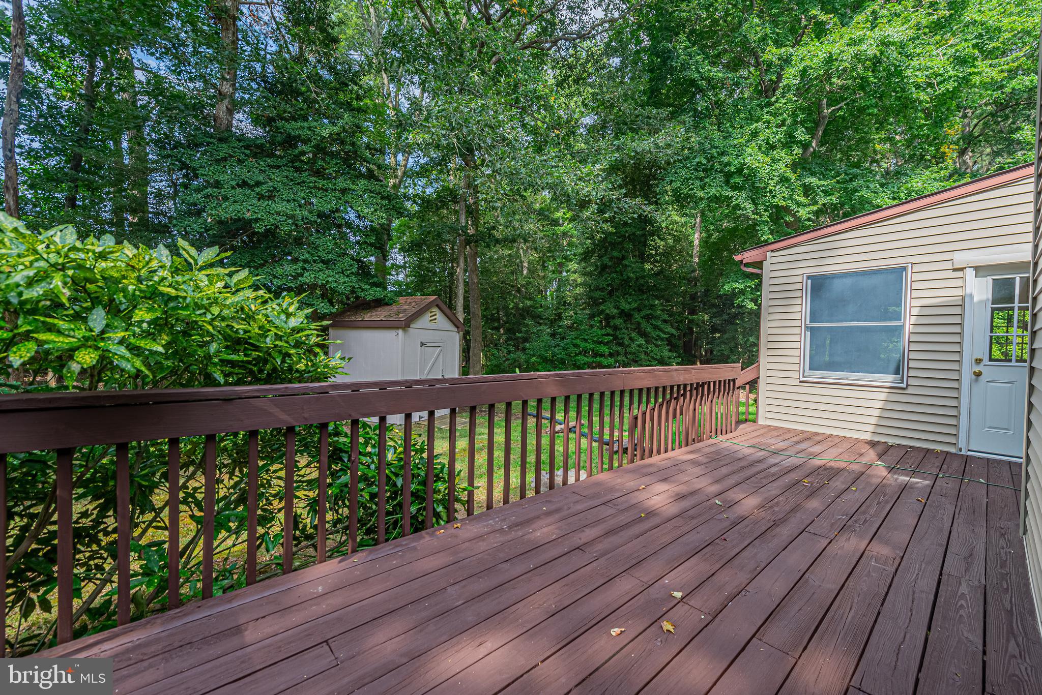 Wood deck beside the house, with brown railings and a leafy wooded yard beyond.