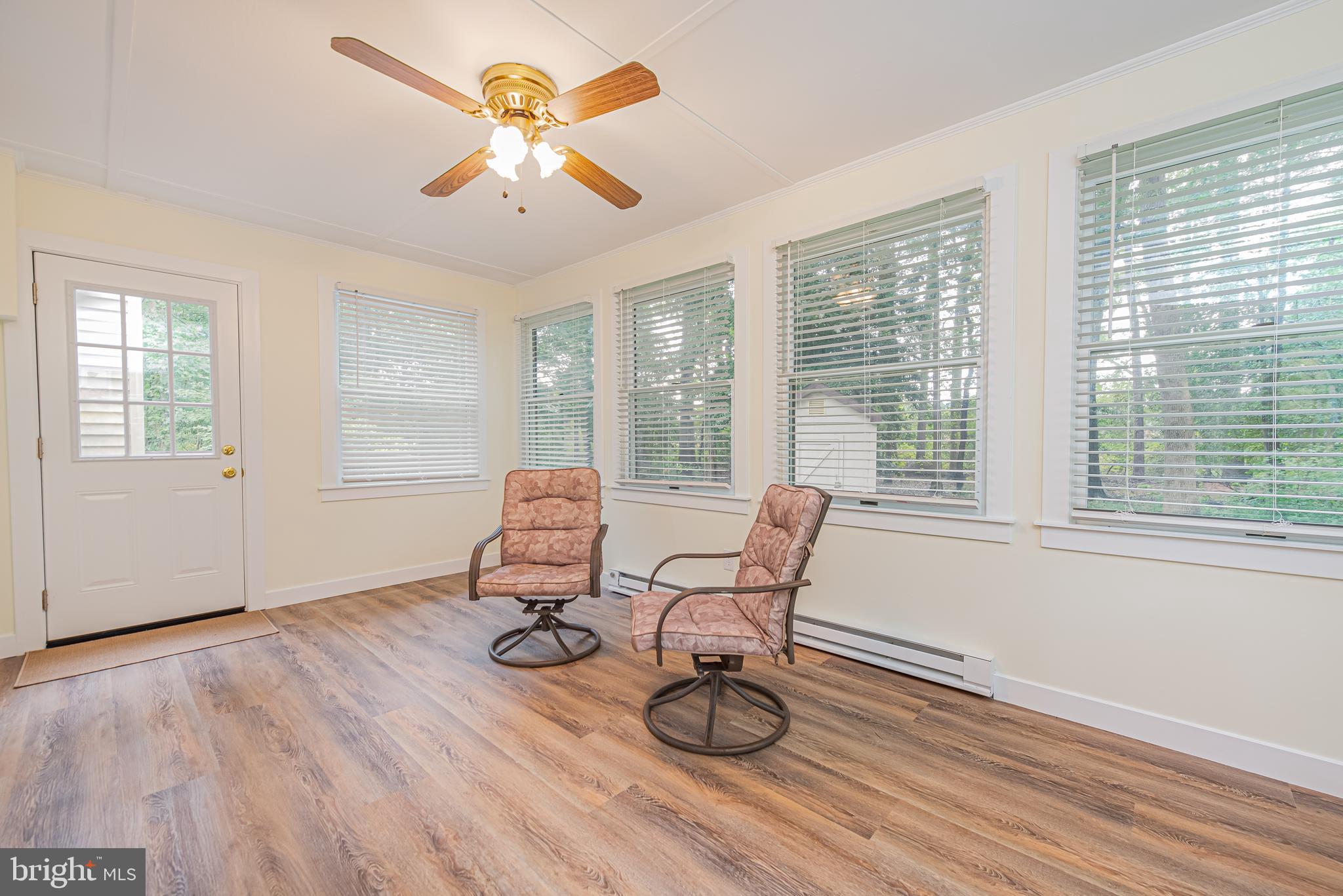 Sunroom with two cushioned chairs, a ceiling fan, and large windows with blinds.