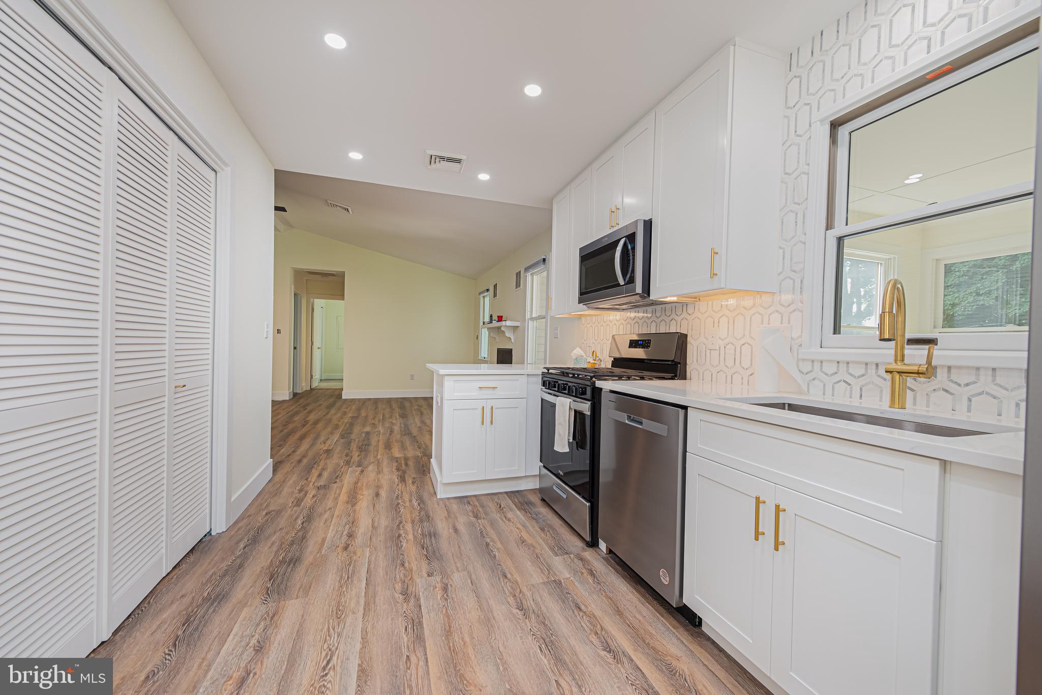 Kitchen with white cabinetry, gold fixtures, geometric tile backsplash, and stainless steel appliances.