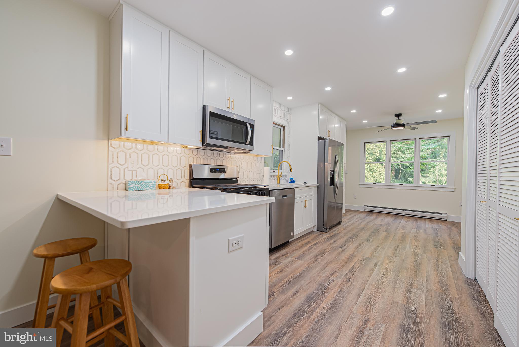 Renovated kitchen with white cabinets, stainless steel appliances, and a large peninsula with wooden stools.