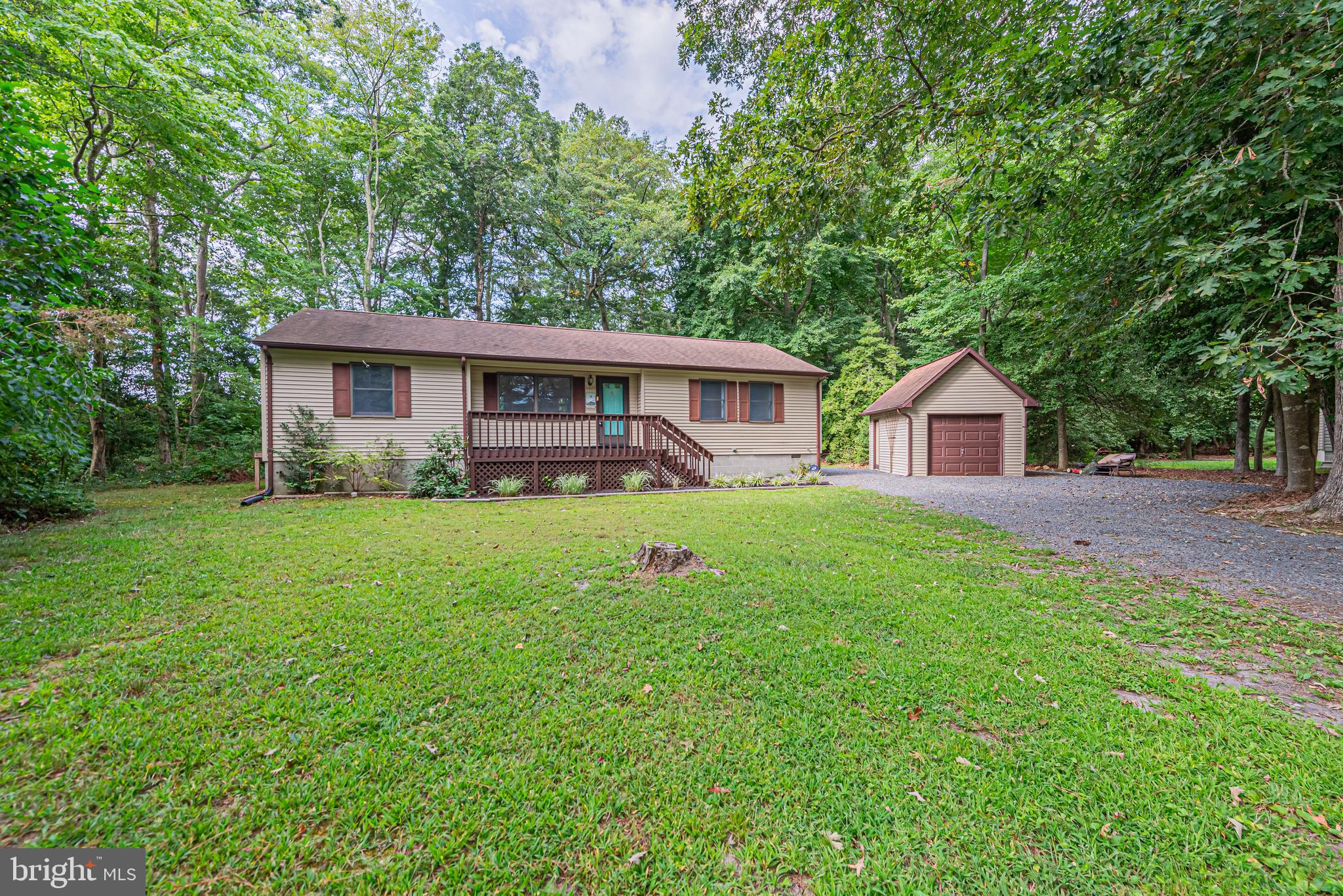 Single-story house with a covered porch and detached garage on a grassy, tree-lined lot.
