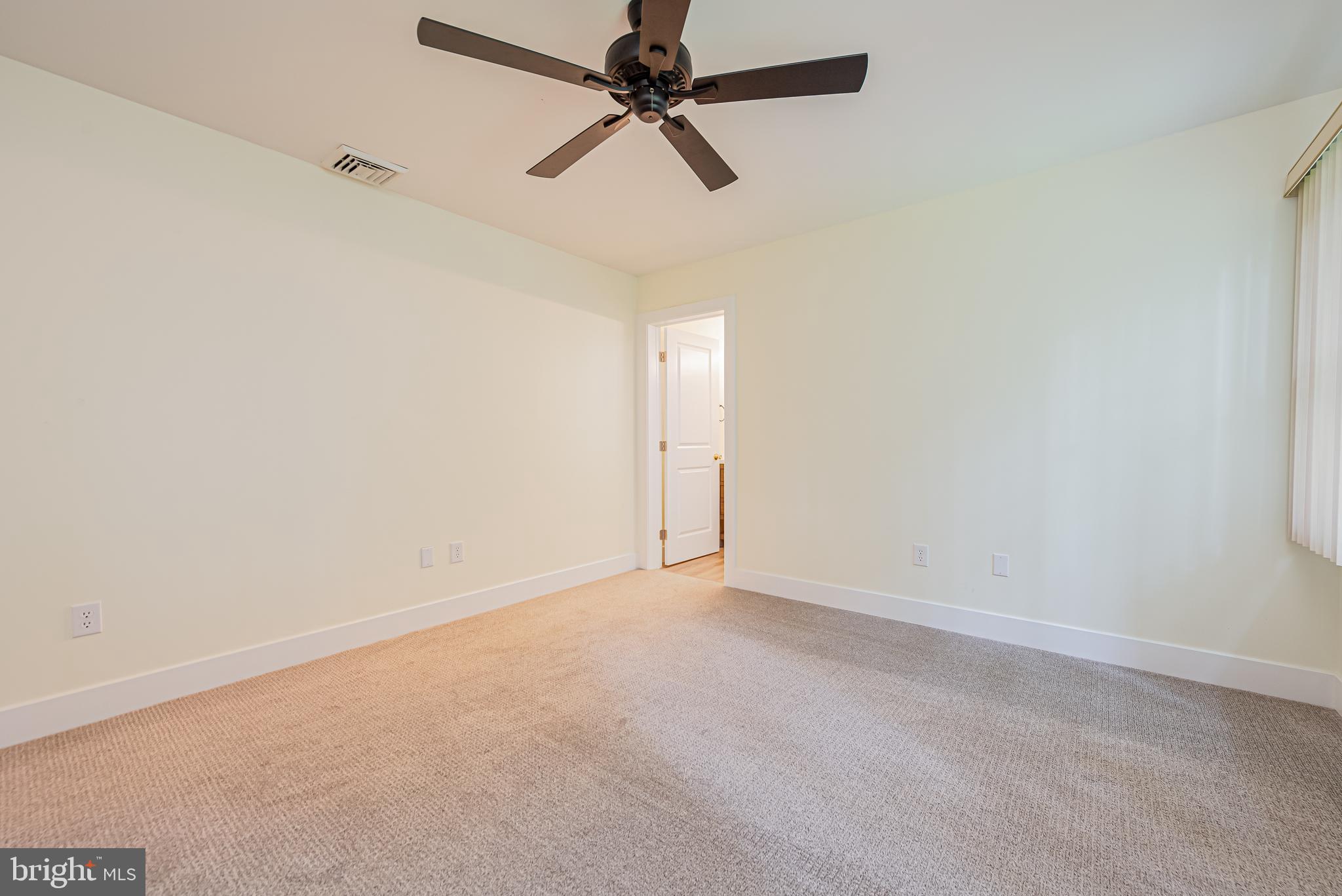 Empty bedroom with beige carpet, a dark ceiling fan, and vertical blinds