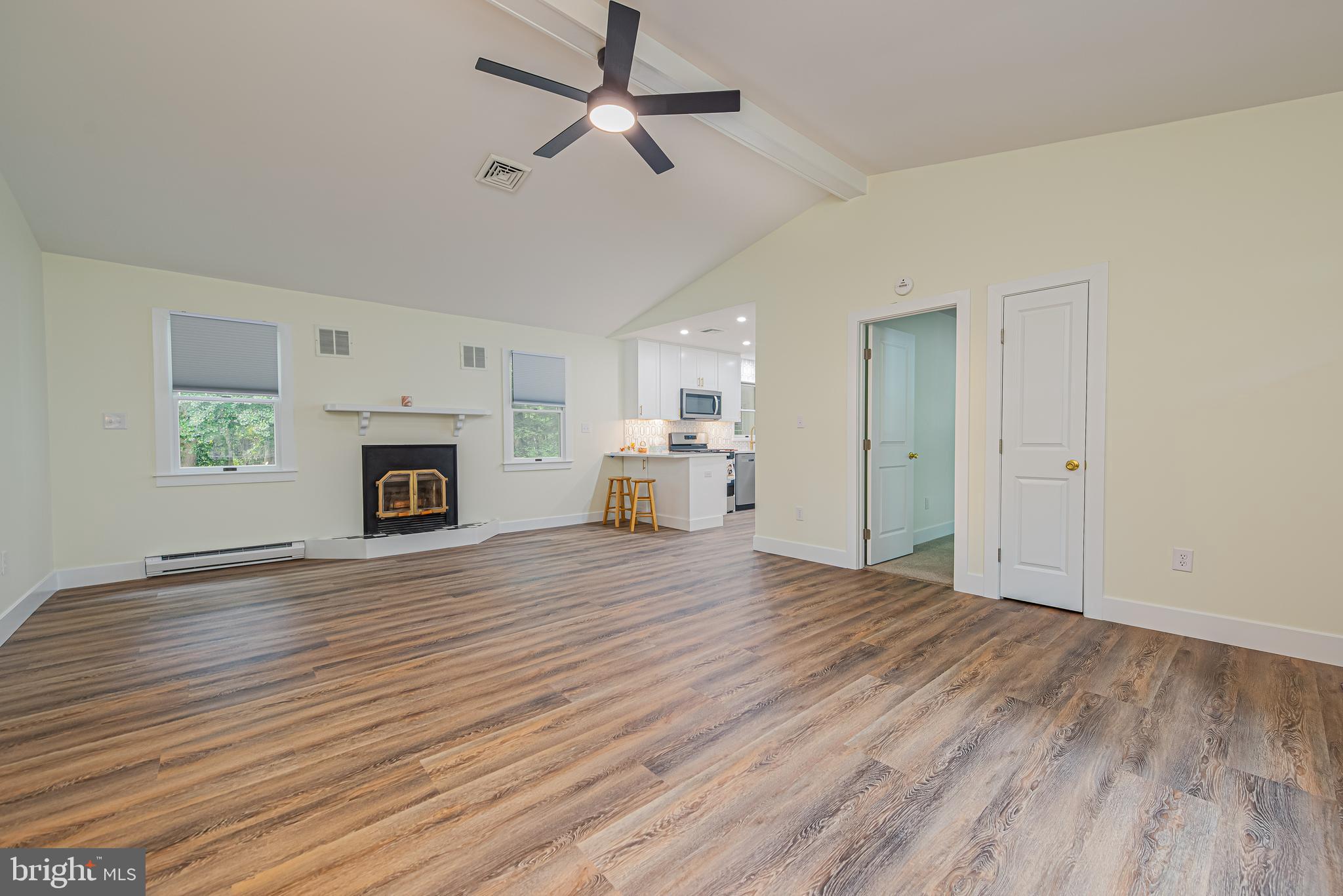 Open living room with vaulted ceiling, wood-look floors, fireplace, and view into the kitchen.