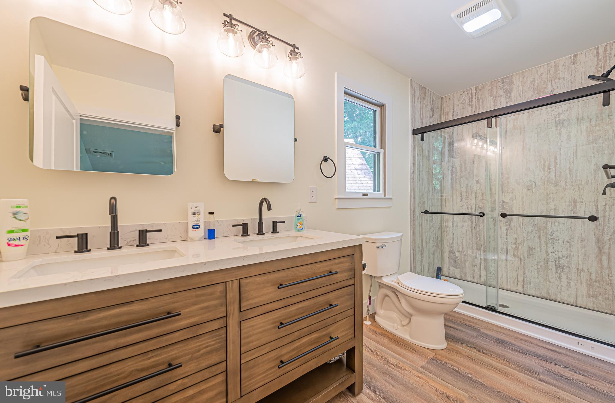 Bathroom with a double-sink wood vanity and glass-enclosed shower with textured walls.